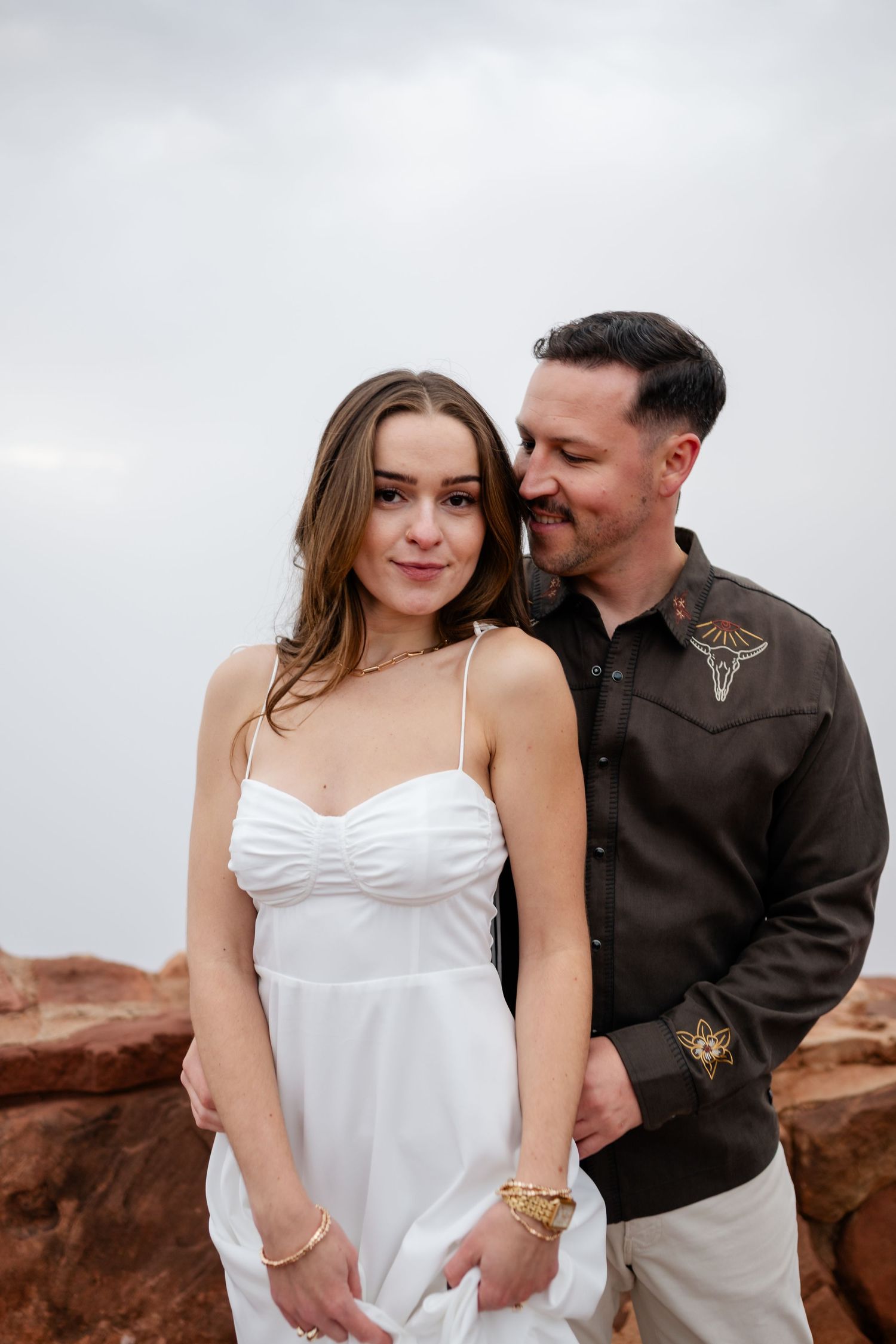 Intimate portrait of couple in white dress and western shirt against desert backdrop.