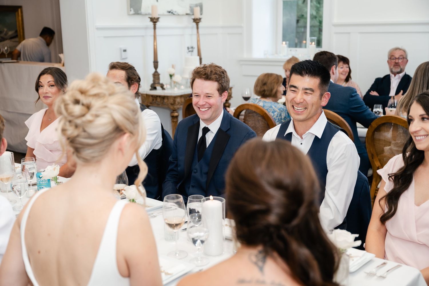 Wedding reception guests laughing and celebrating at elegant white venue.