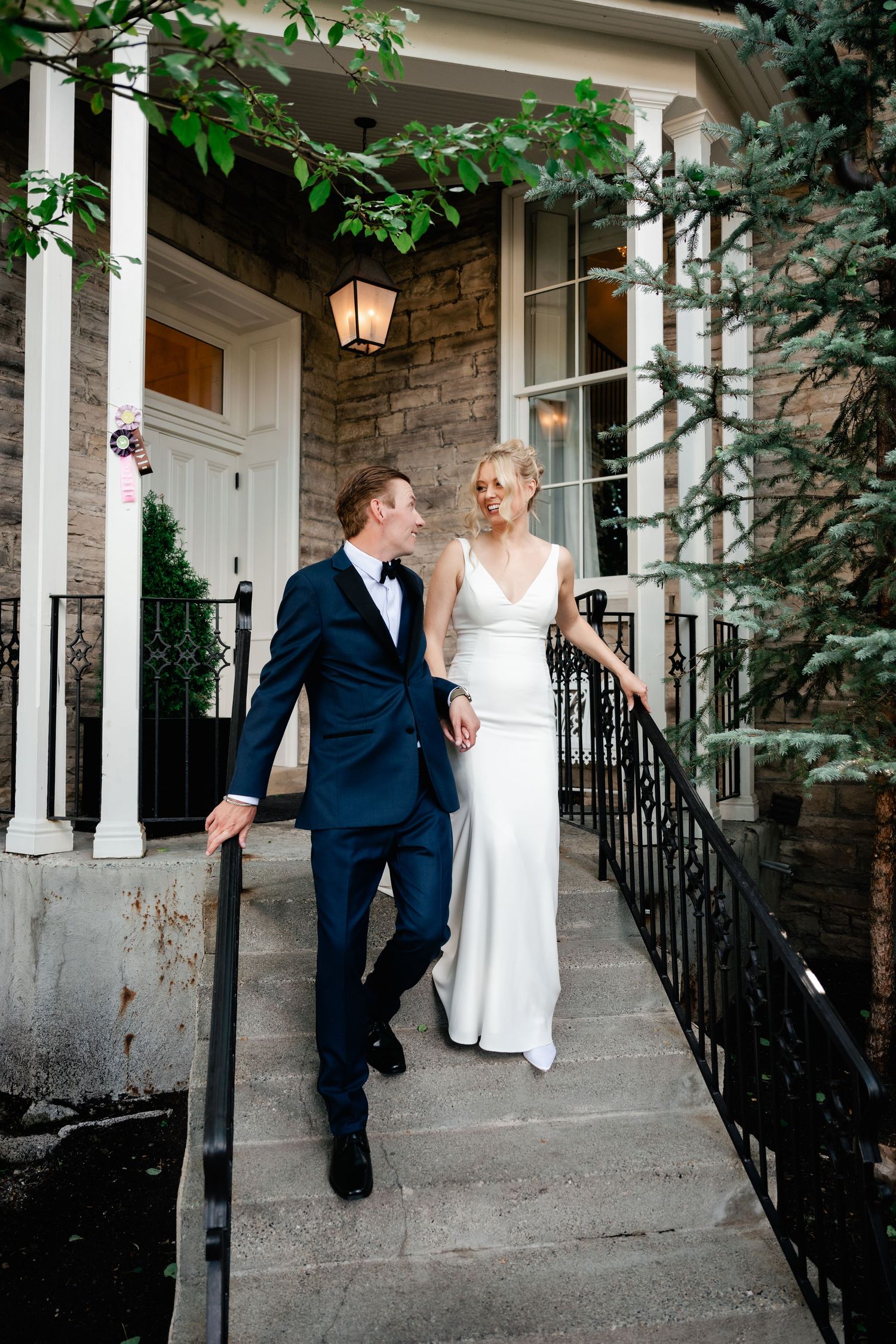 A couple shares a romantic moment on the porch of a historic stone building with white columns.