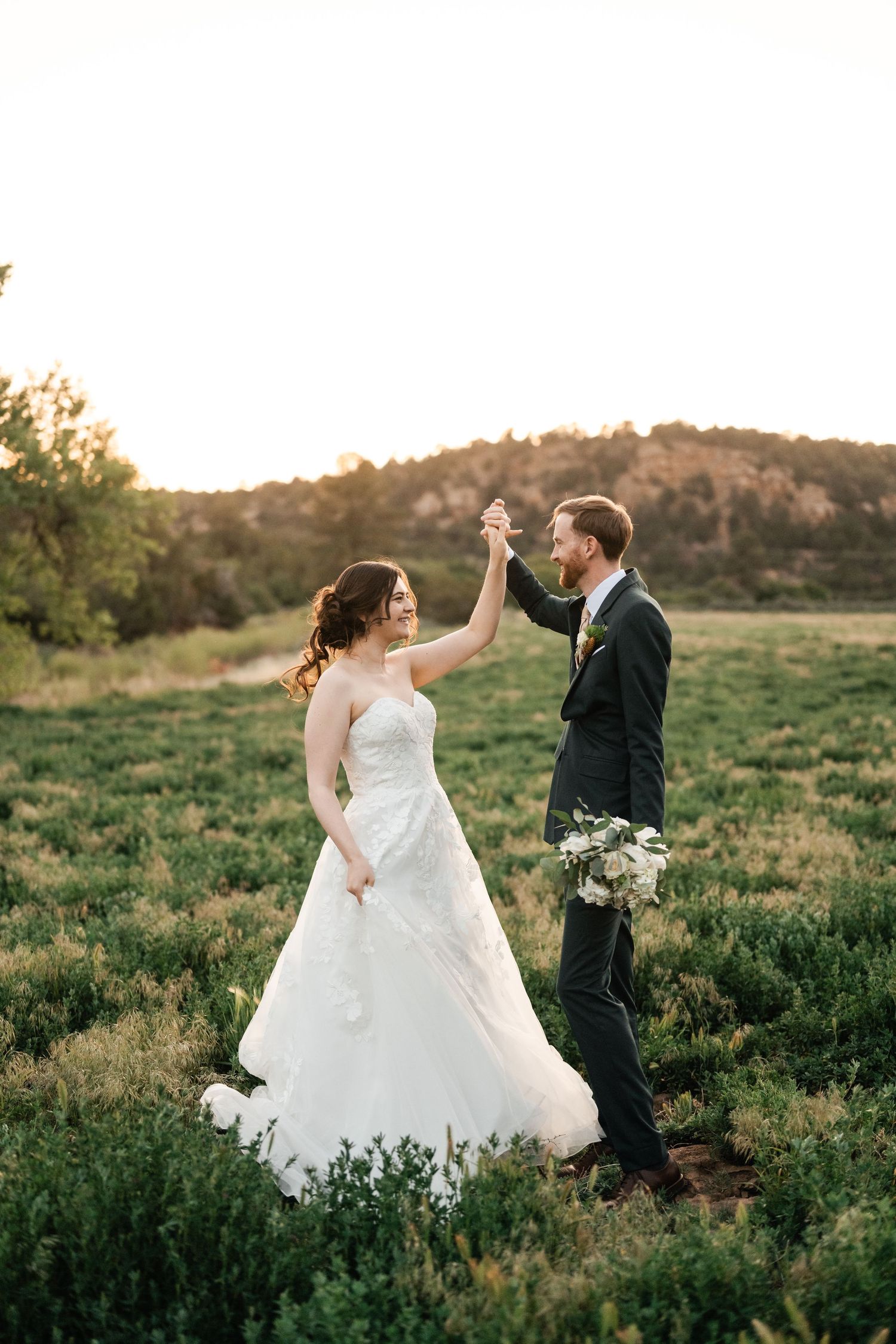 A romantic moment captured in a grassy field with rolling hills at sunset.
