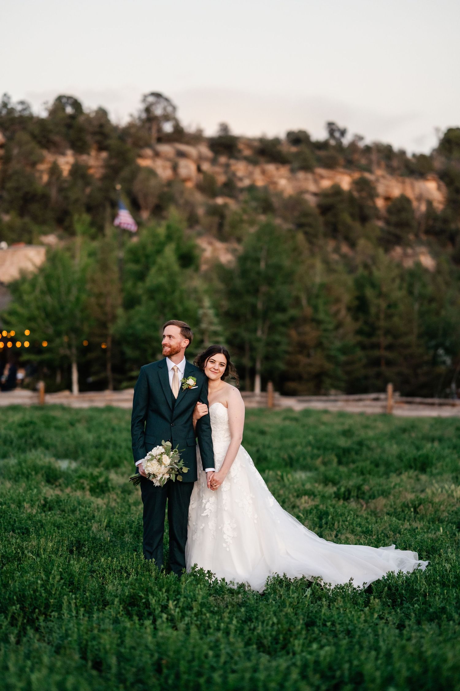 Wedding couple posing in green field with mountain backdrop at sunset.
