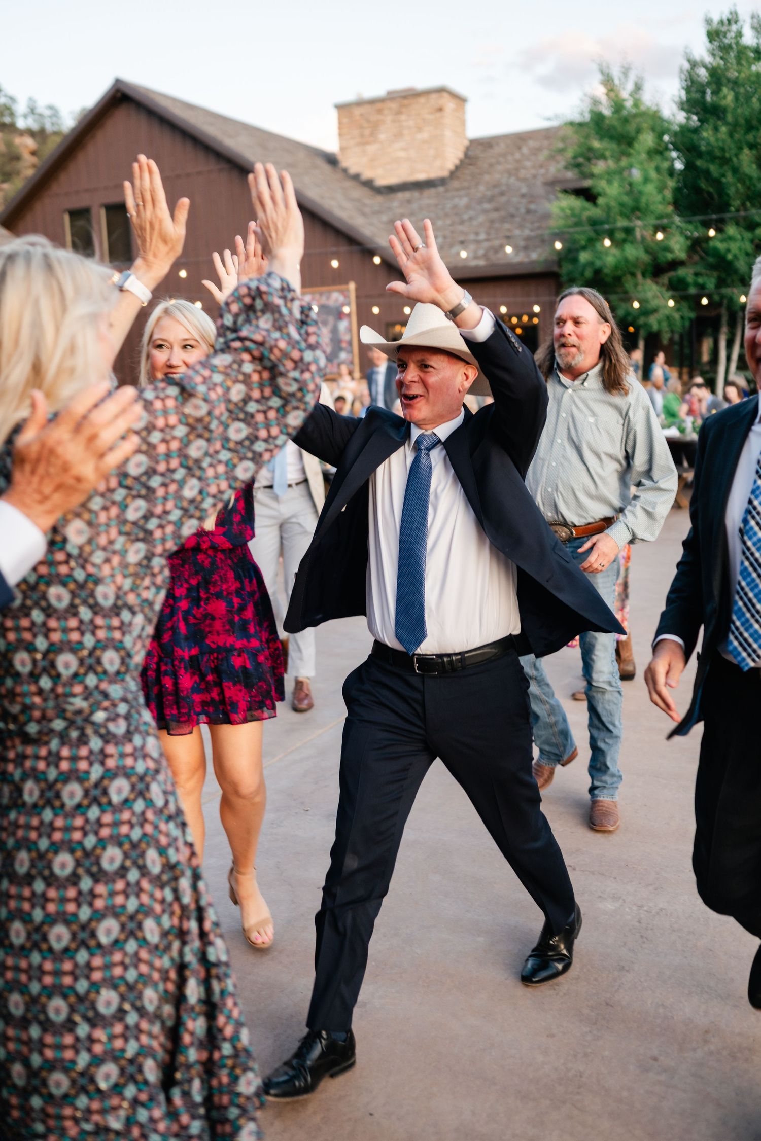 Energetic wedding guests dance and jump with raised arms during the reception celebration.