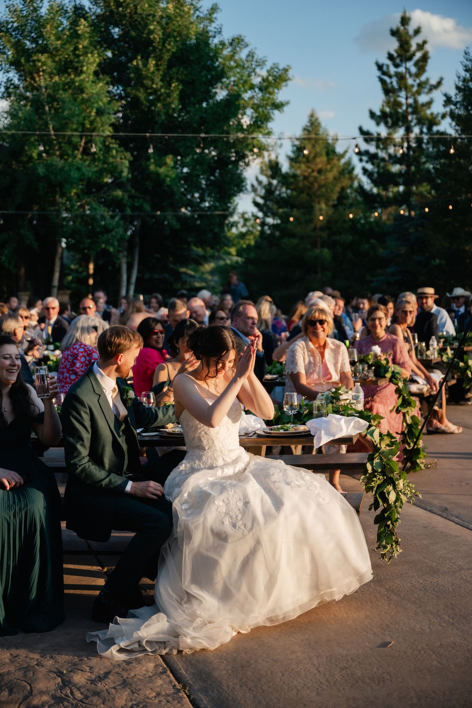 Wedding guests watch as newlyweds perform their first dance on an outdoor patio under evening sunlight.