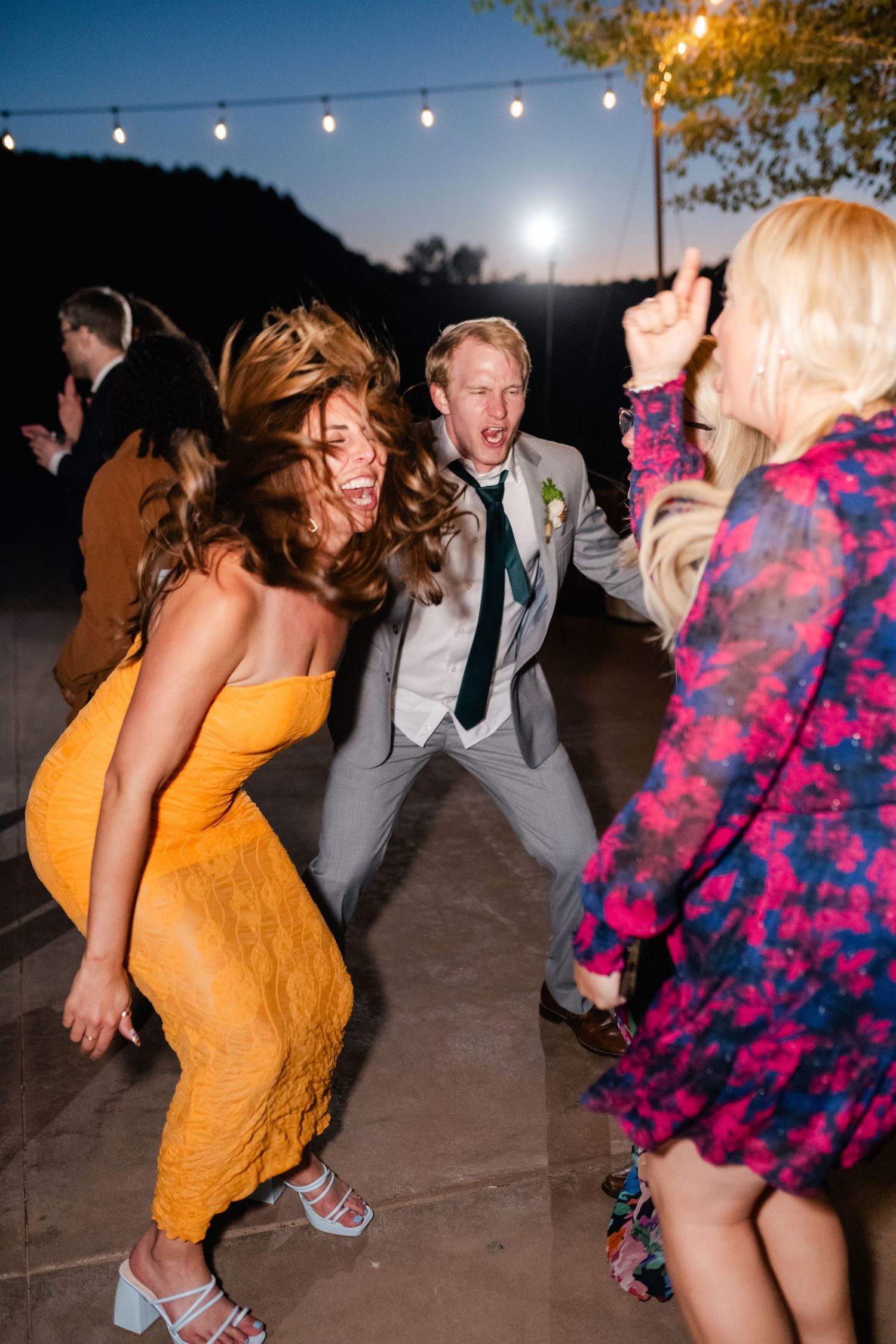 Wedding guests dancing energetically under string lights at an outdoor reception.