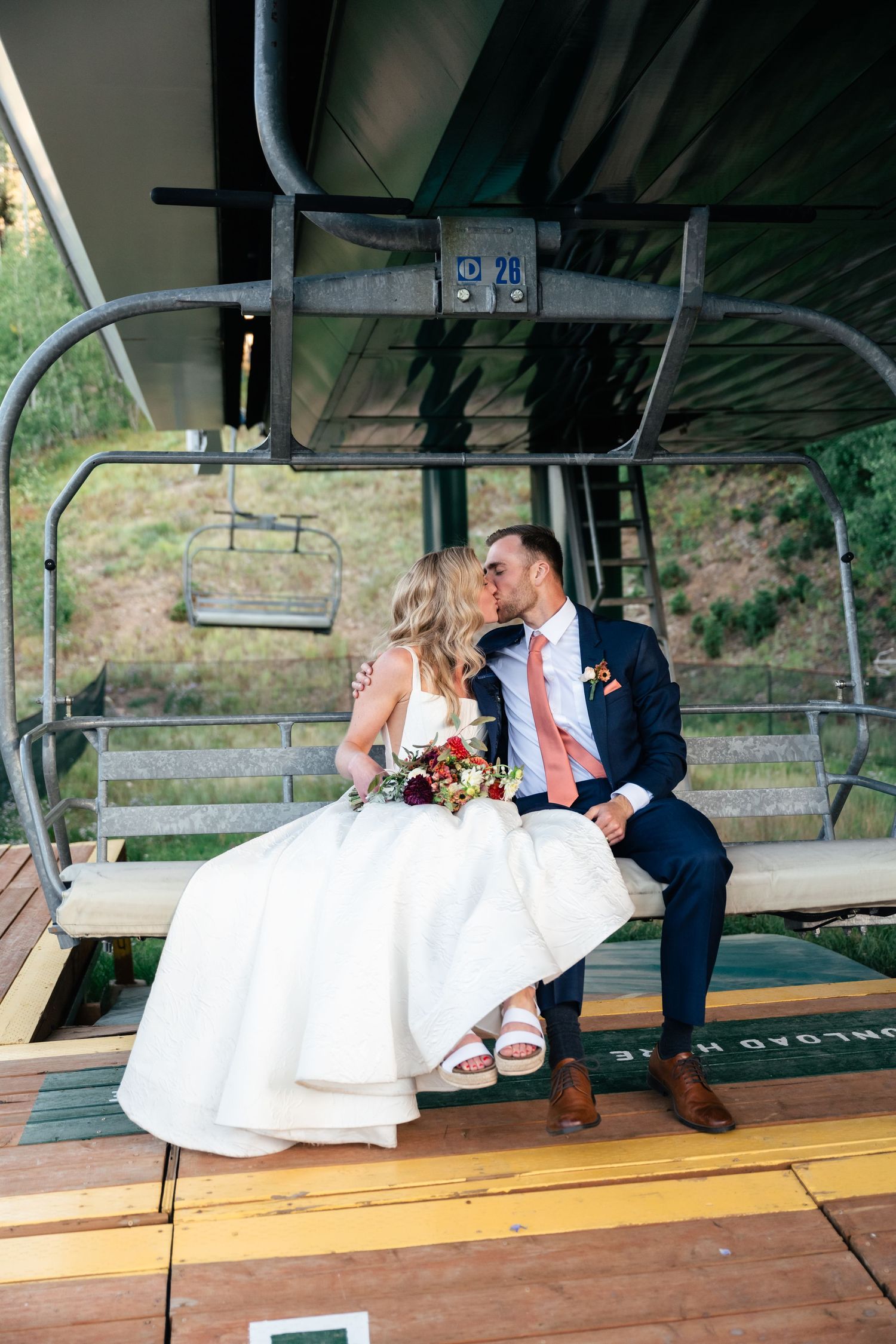 Couple relaxing on wooden ski lift bench during summer wedding photo session.