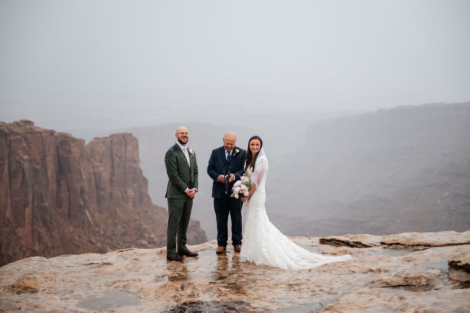 Wedding ceremony unfolding on dramatic canyon overlook with misty desert backdrop.