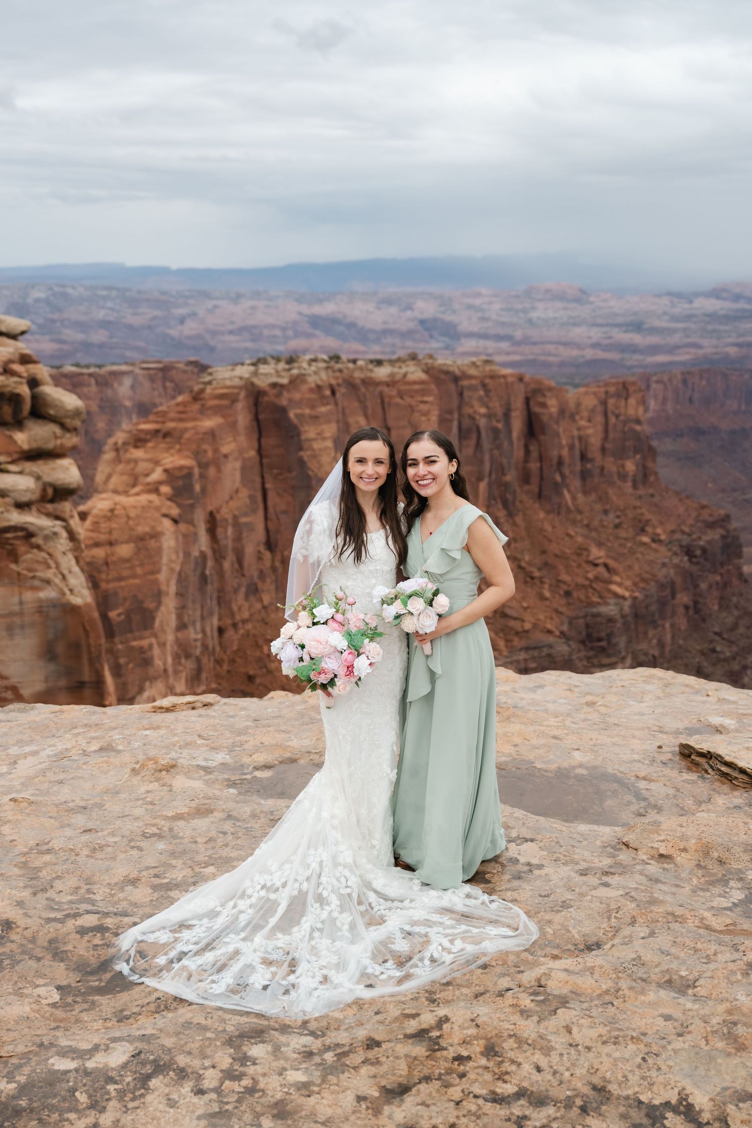 Two people in wedding attire share intimate moment on cliff edge with dramatic canyon backdrop.