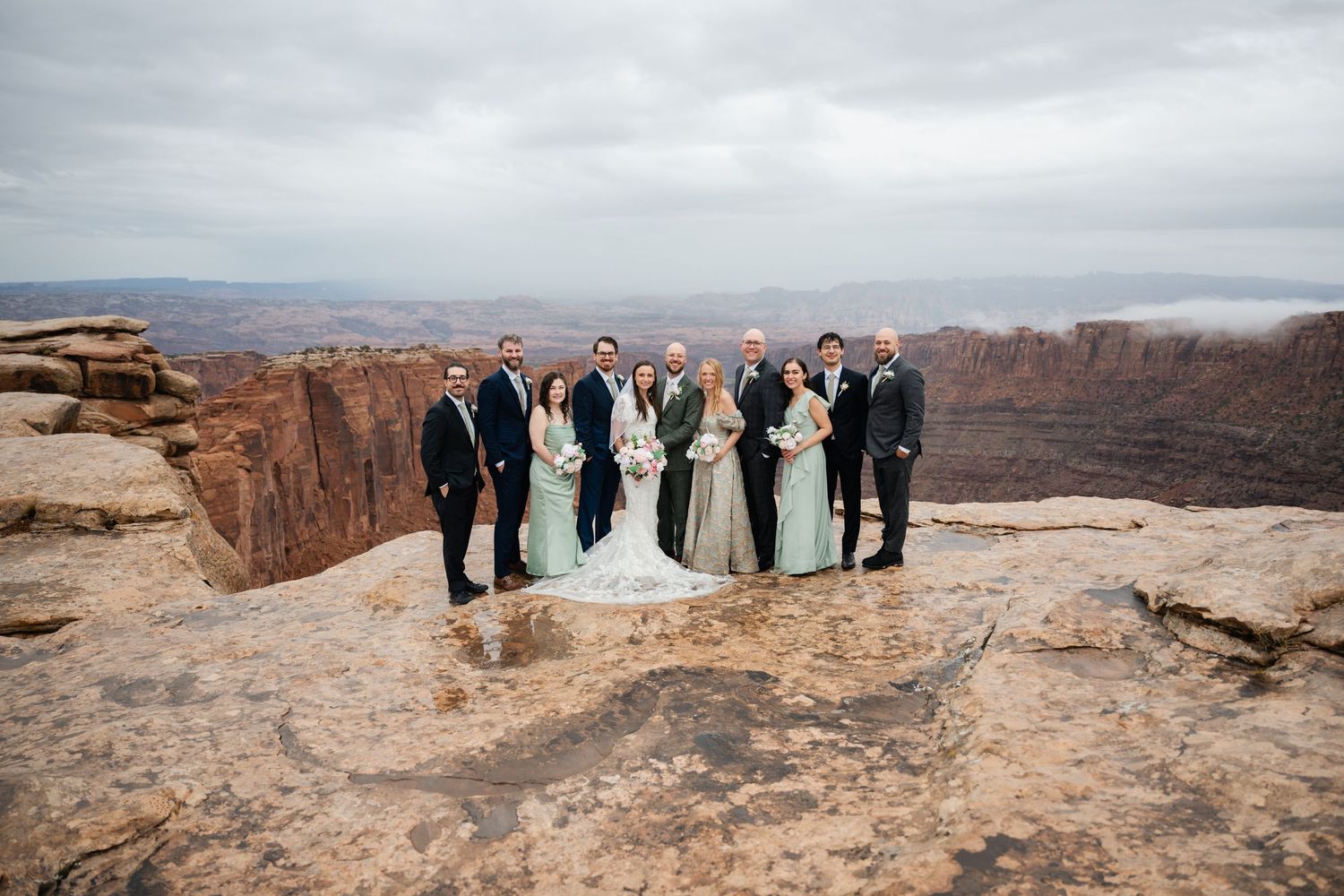 Wedding party stands on dramatic red rock cliff edge at Dead Horse Point State Park in Utah.