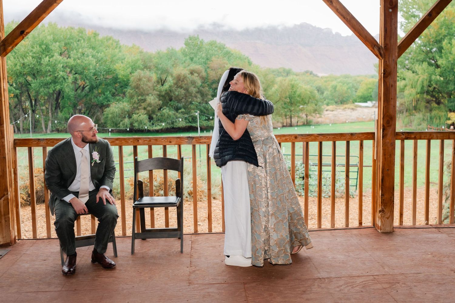 Couple dancing together in a rustic wooden pavilion overlooking scenic mountain landscape.