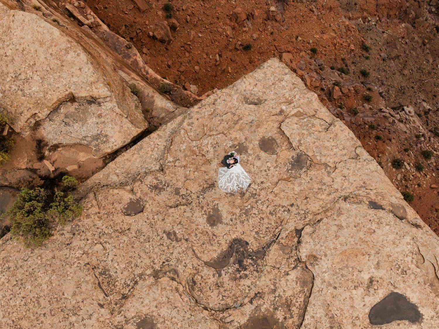 A person in white clothing stands on a large beige rock formation against a reddish desert landscape.