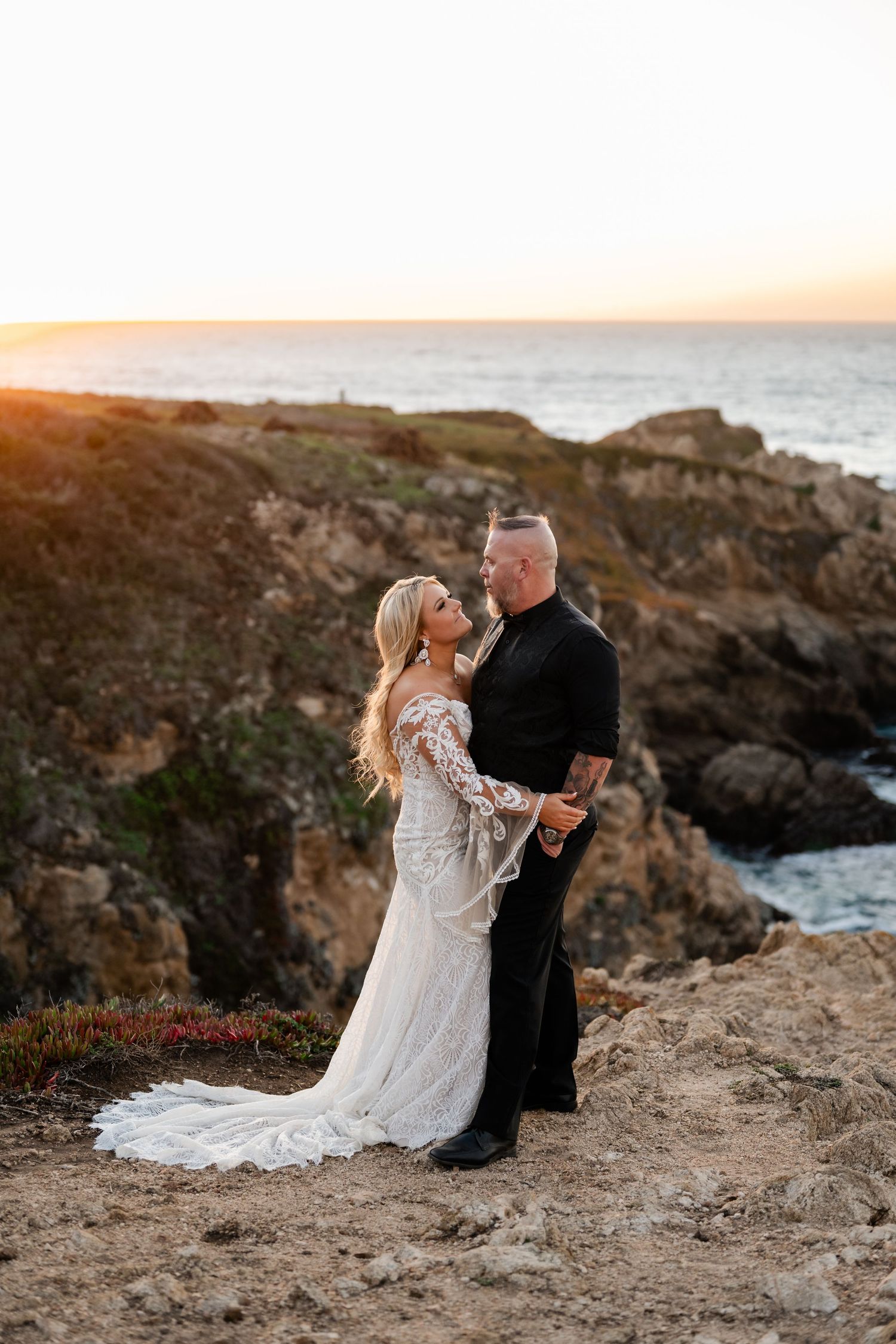 Wedding couple embracing on rocky coastal cliffs during sunset.