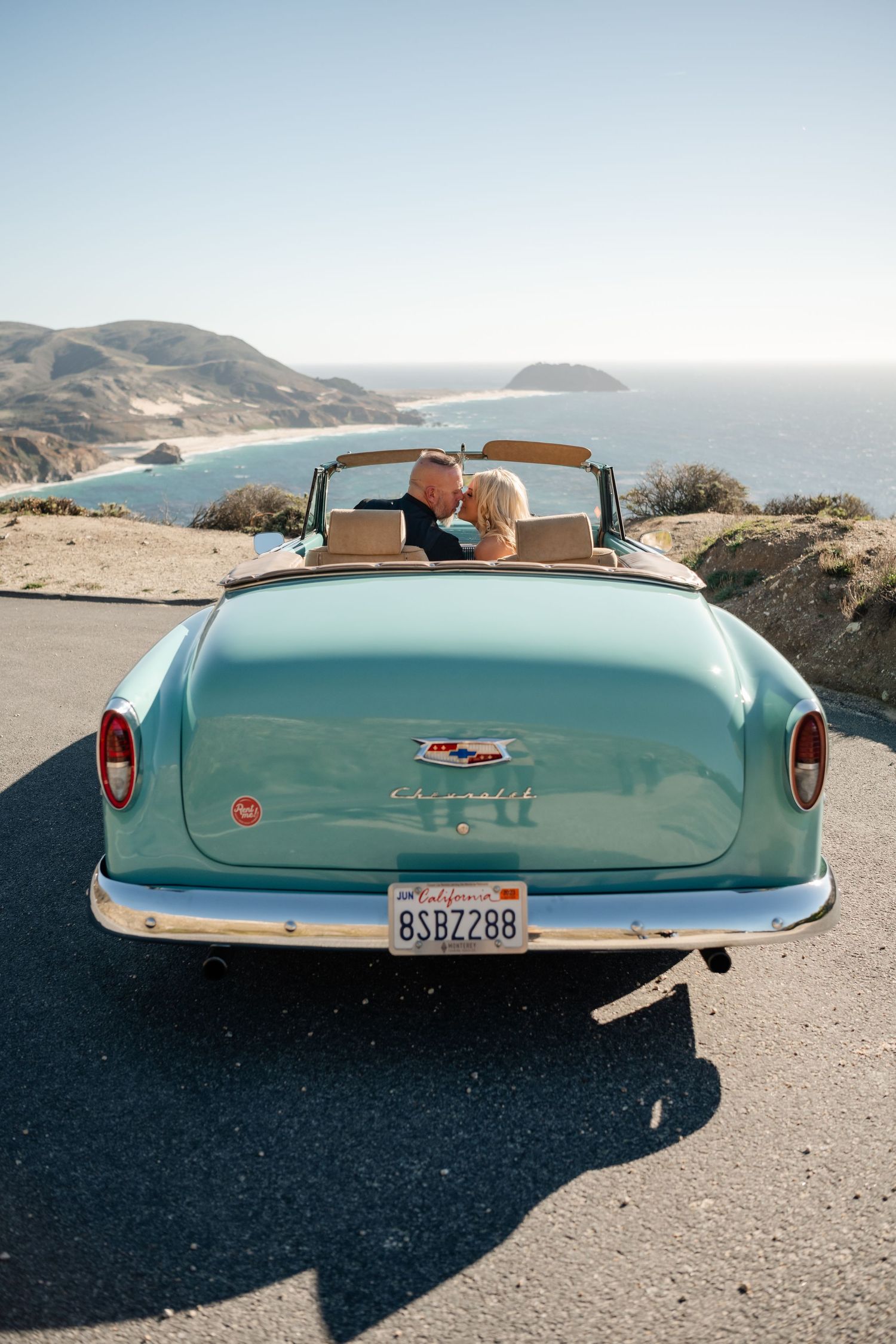 Turquoise vintage Chevrolet convertible parked along scenic coastal highway.
