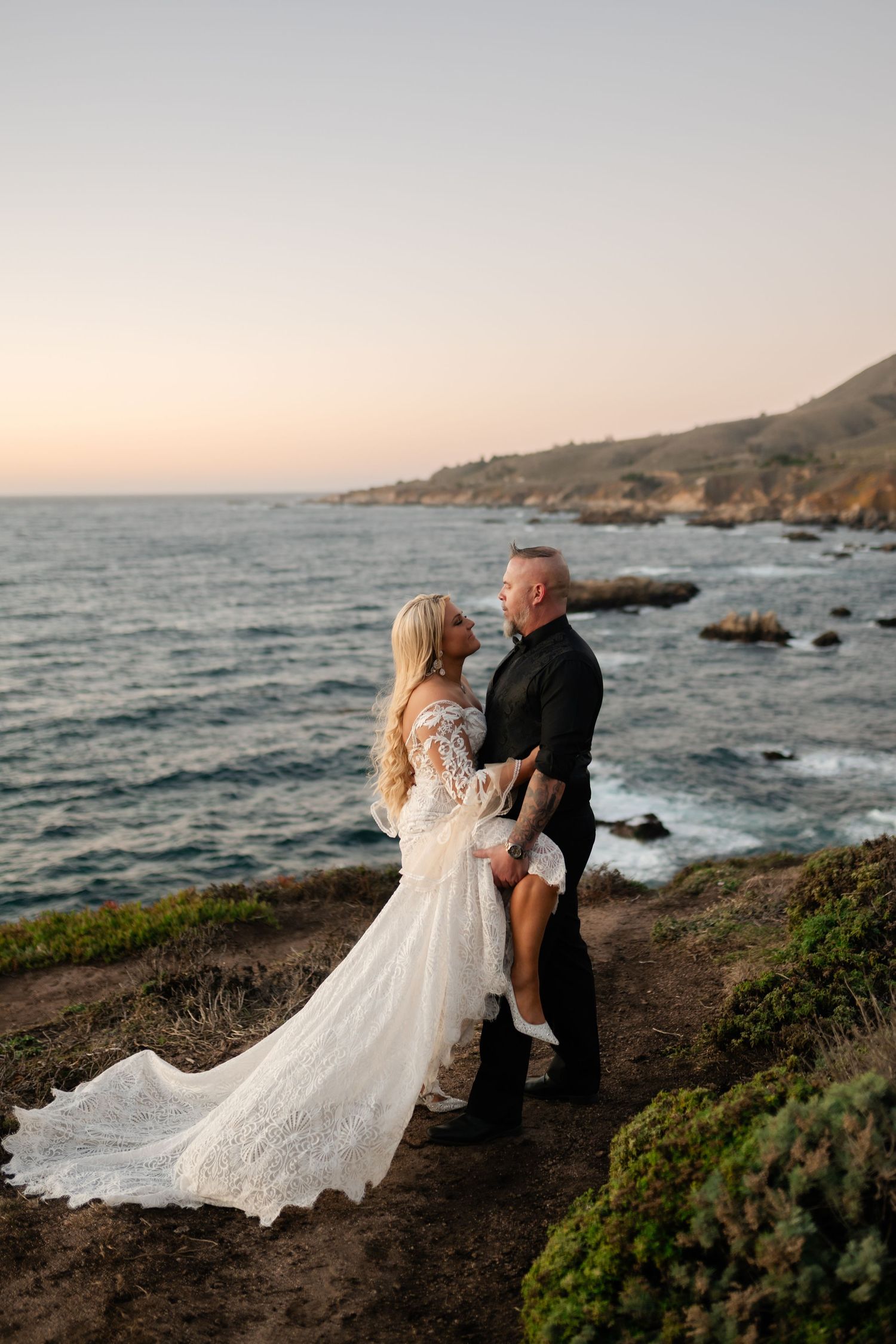 Wedding couple embracing on rocky coastline during golden hour.
