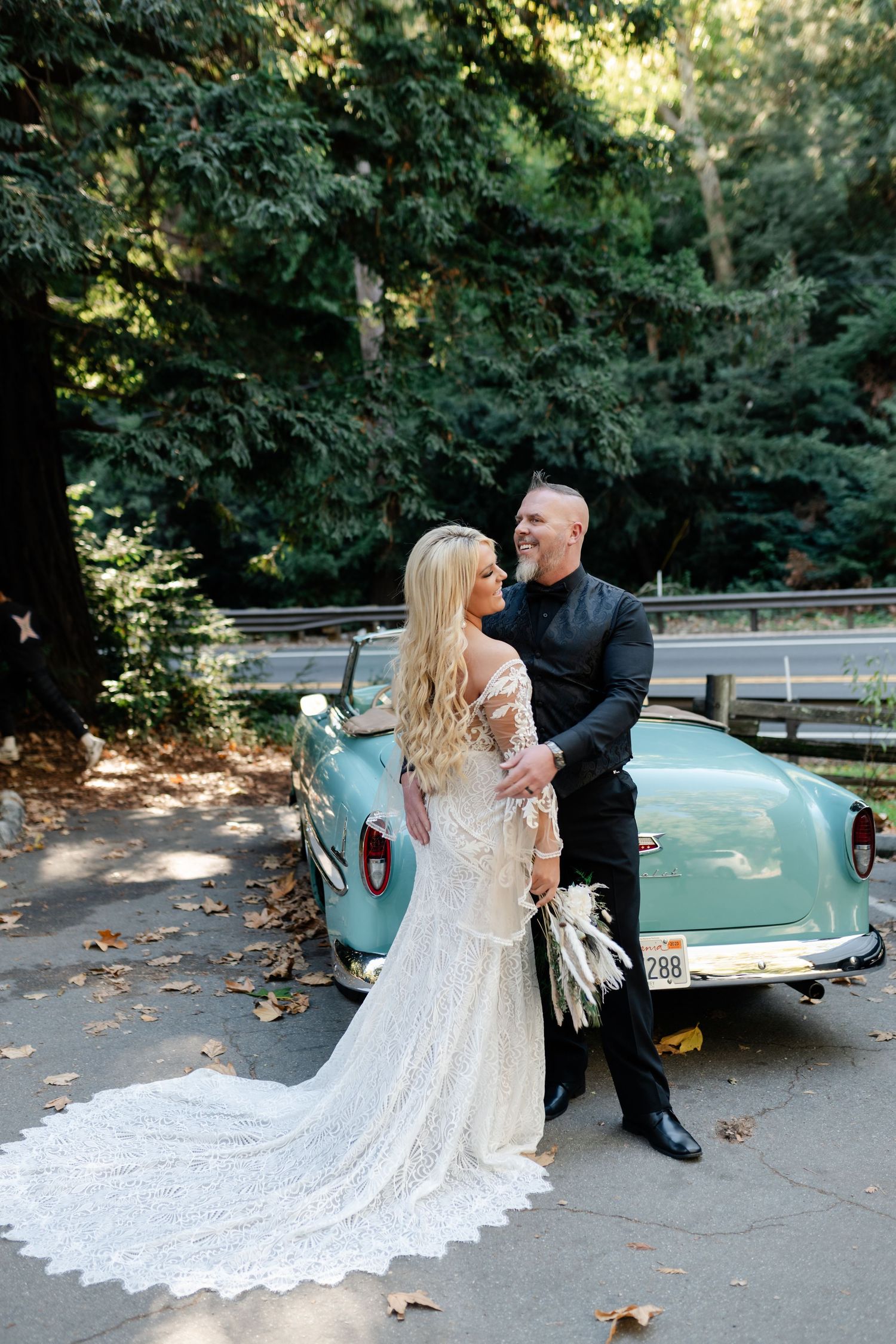 A romantic wedding portrait with a vintage light blue car in a forest setting.