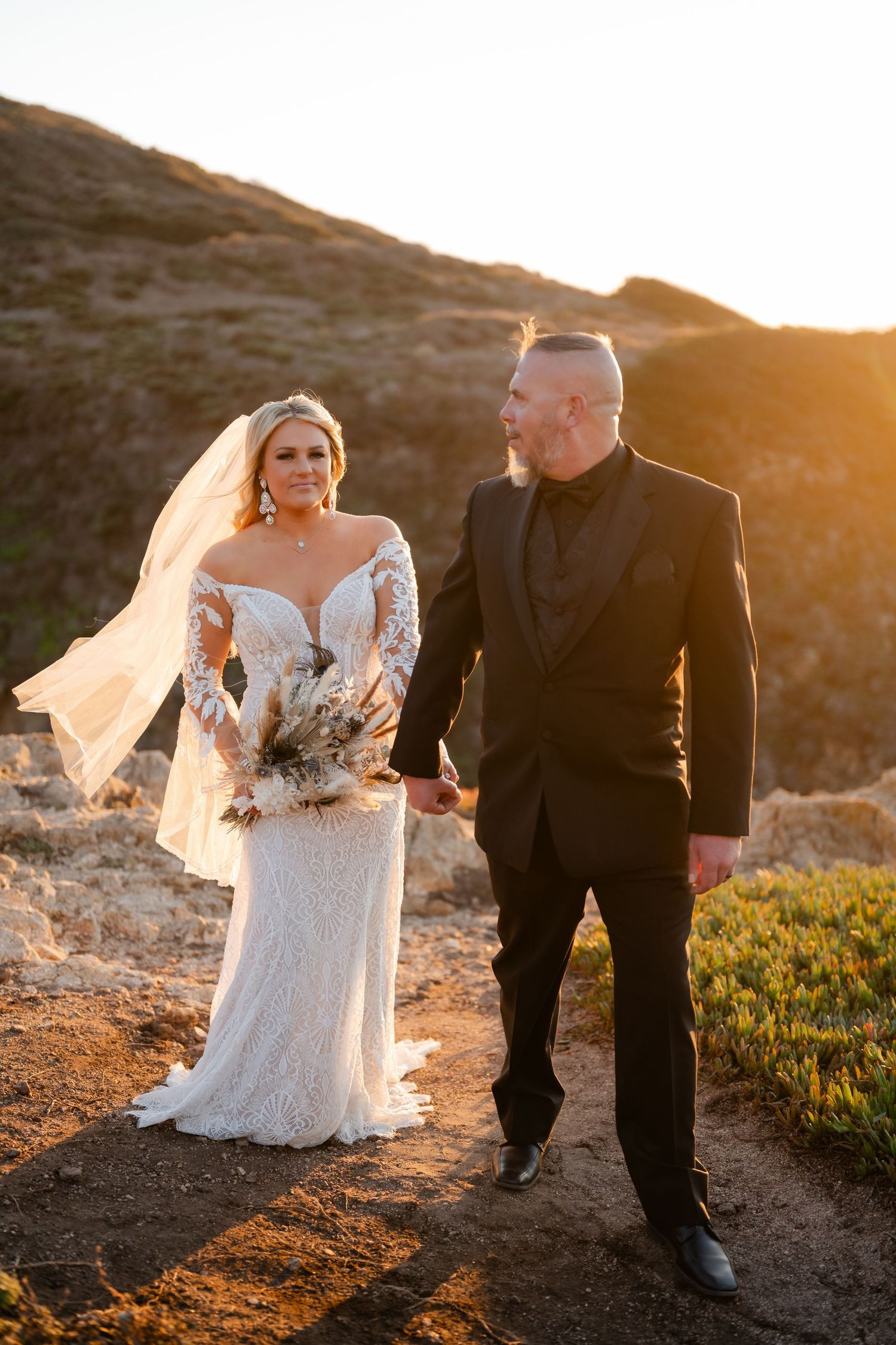 Wedding couple walking together on coastal cliffs during golden hour sunset.