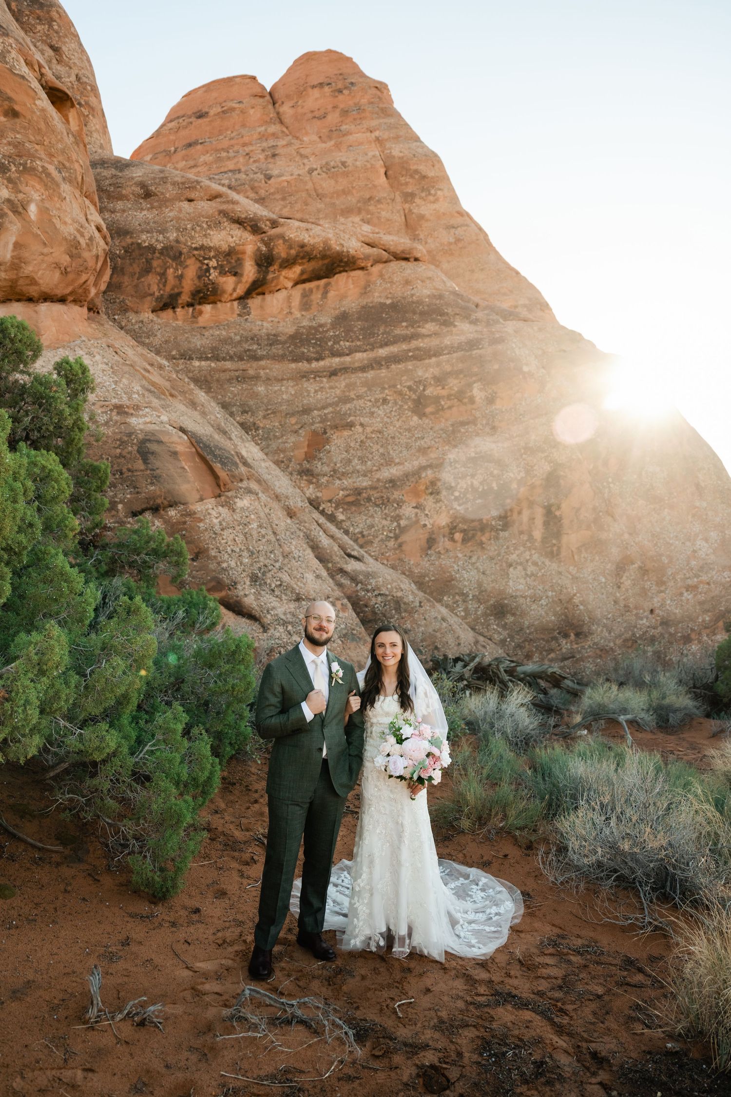Newlyweds pose together at sunset among majestic red rock formations in the desert.