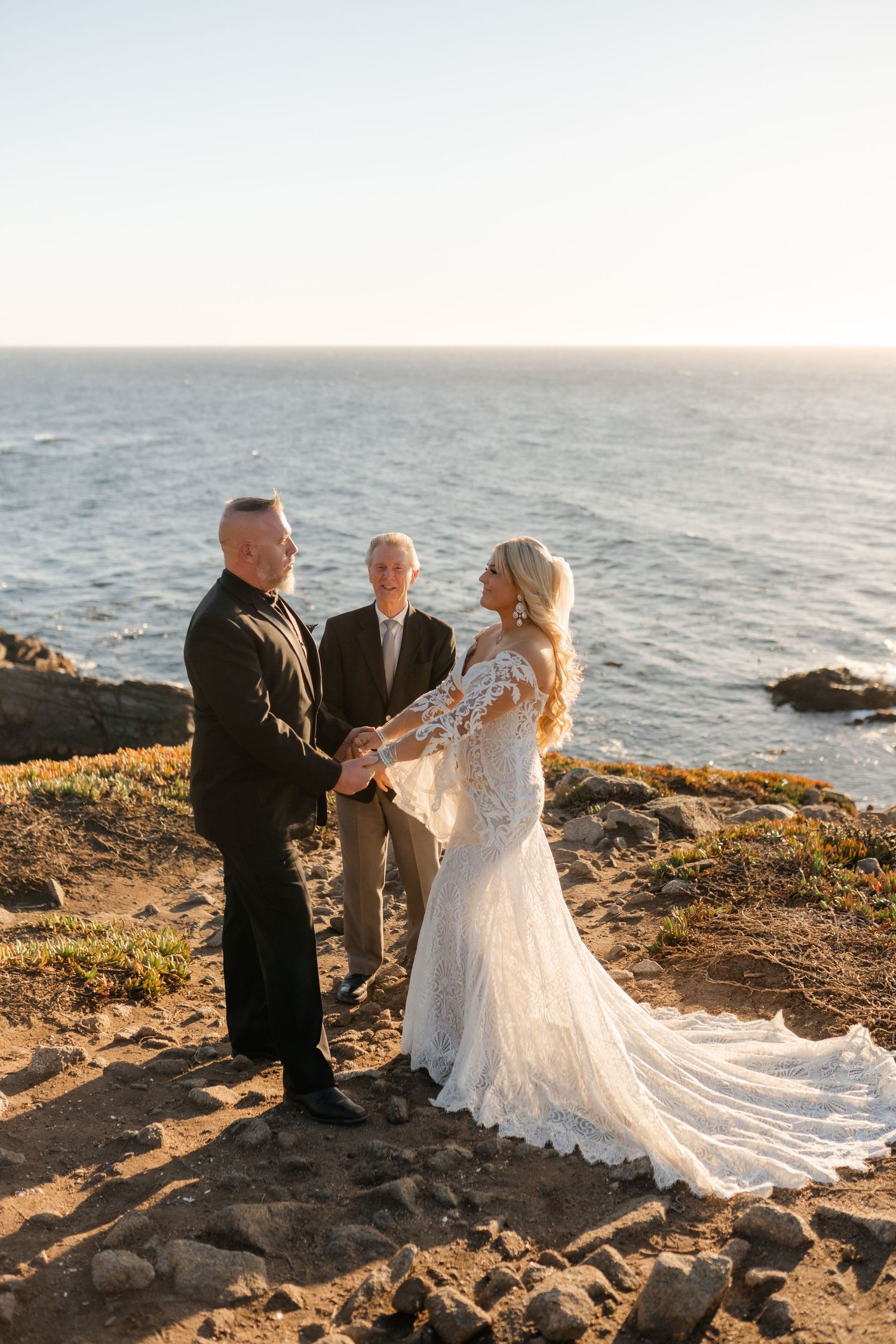 A wedding ceremony takes place on a dramatic coastal cliff at golden hour with the ocean as a stunning backdrop.
