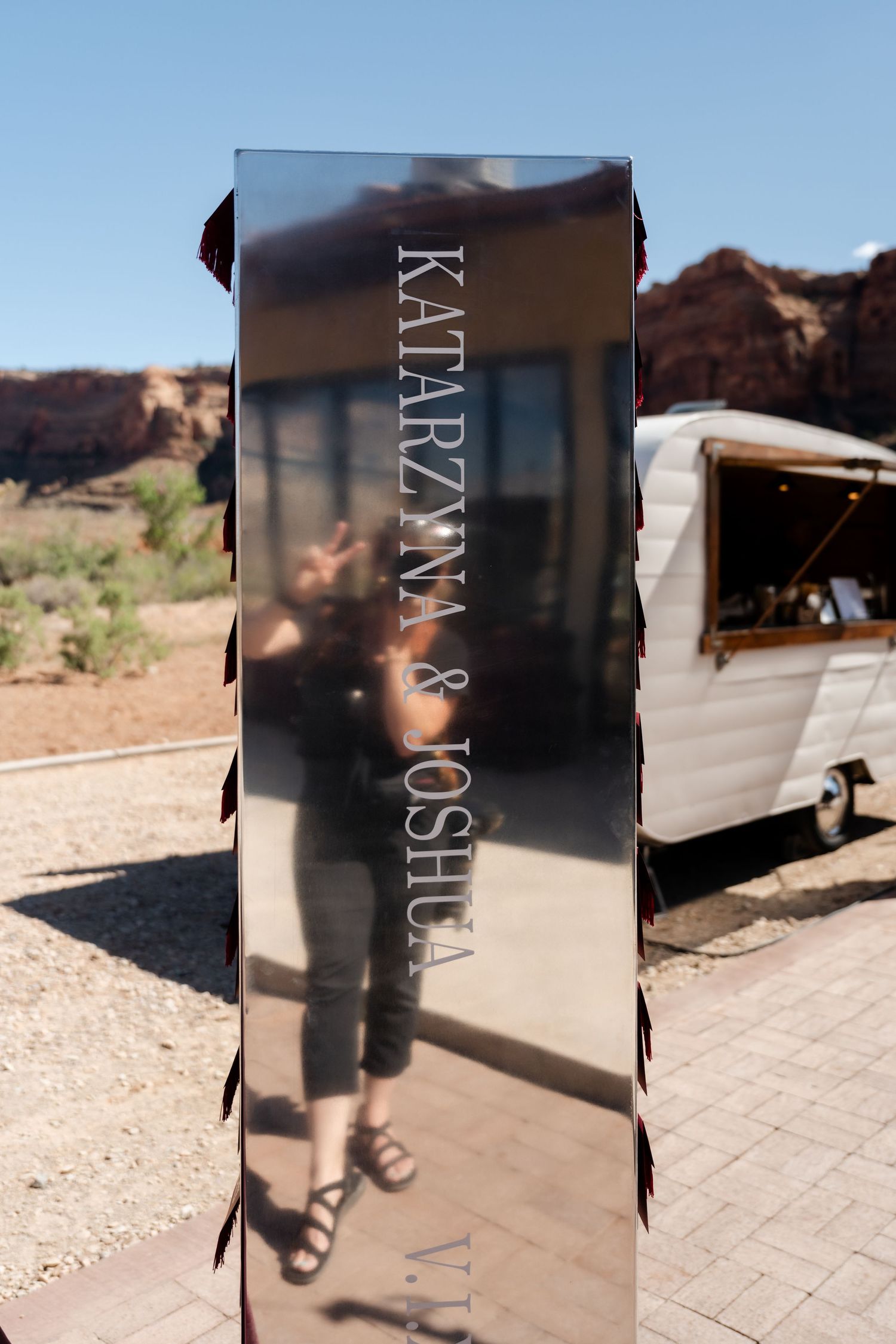 Mirrored wedding sign reading Katarzyna and Joshua in desert landscape with vintage trailer and red rocks.