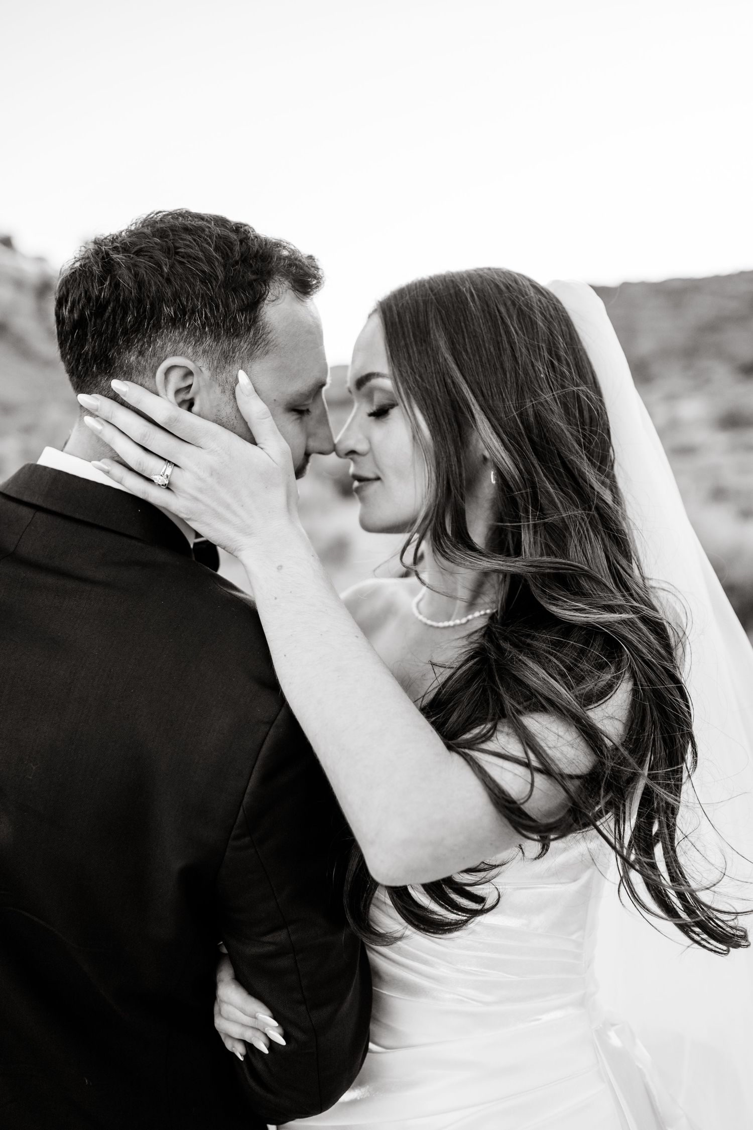 Black and white close-up of bride and groom sharing an intimate moment, bride in veil touching grooms face tenderly.