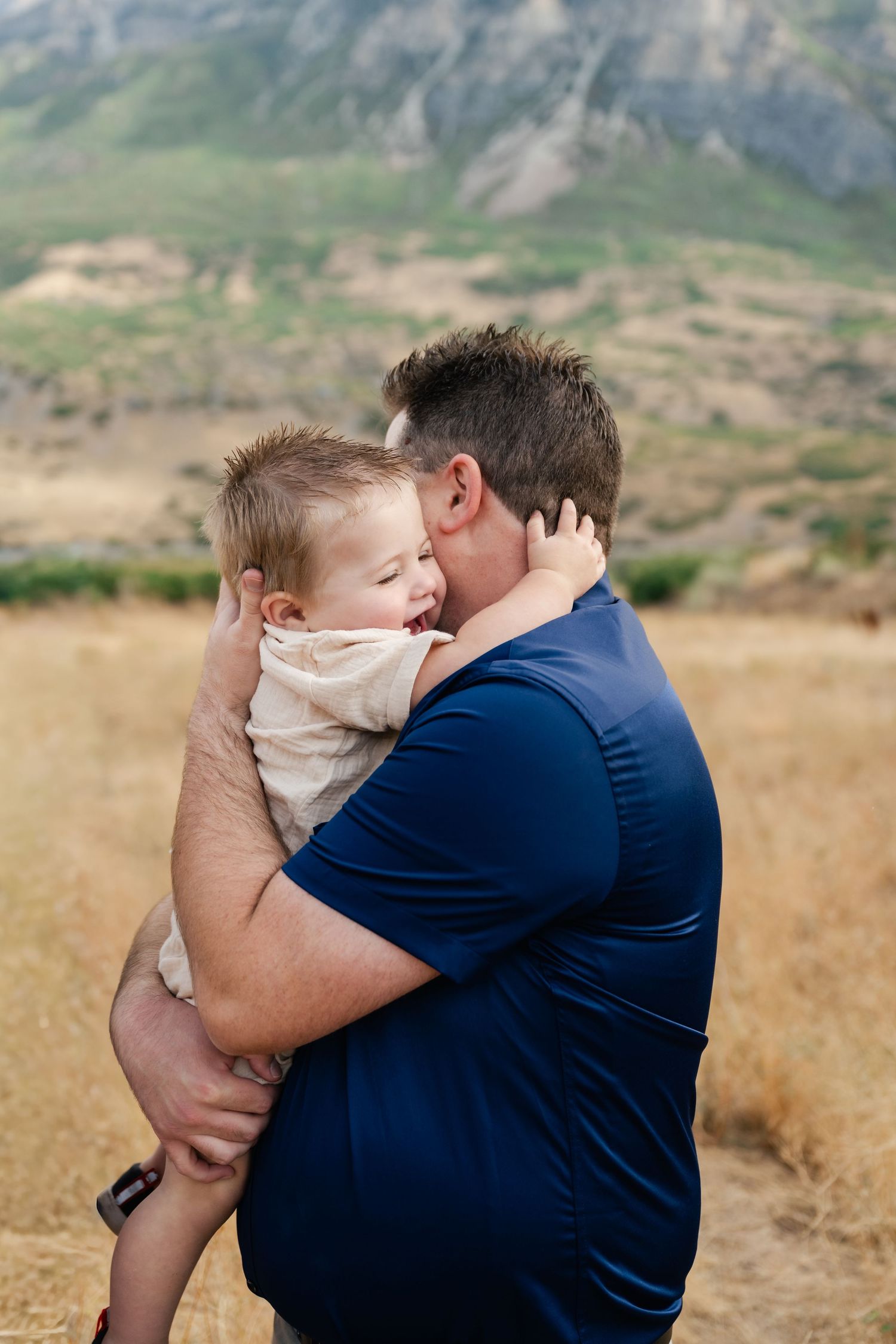 A tender moment between parent and child embracing against a mountainous backdrop in nature.
