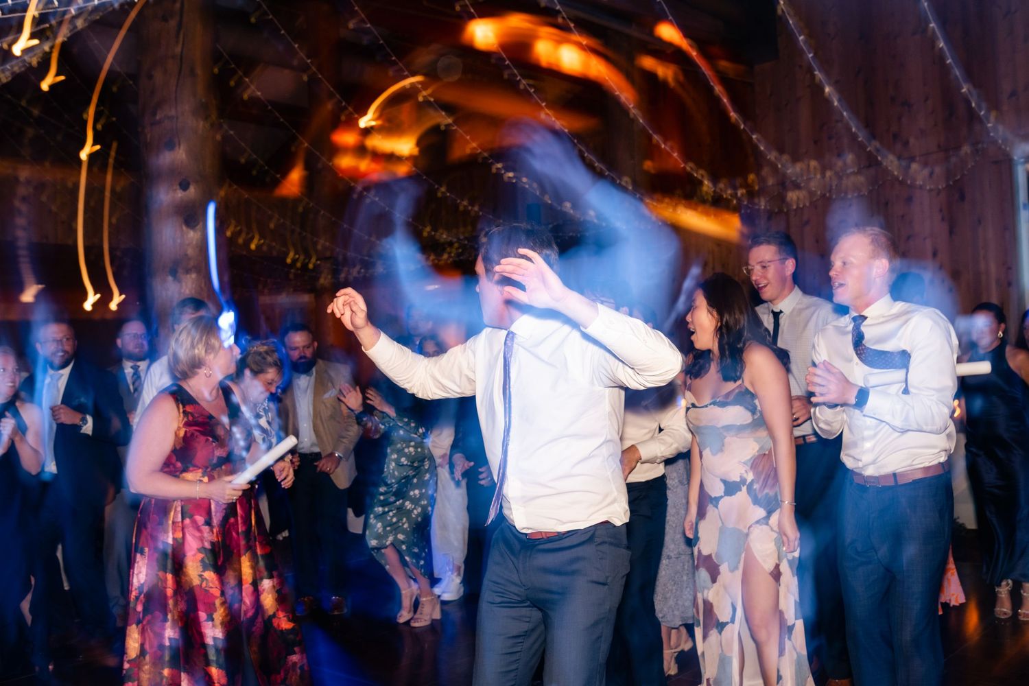 Party guests dancing at a wedding reception with motion blur and colorful lighting effects creating an energetic atmosphere. Utah Wedding.