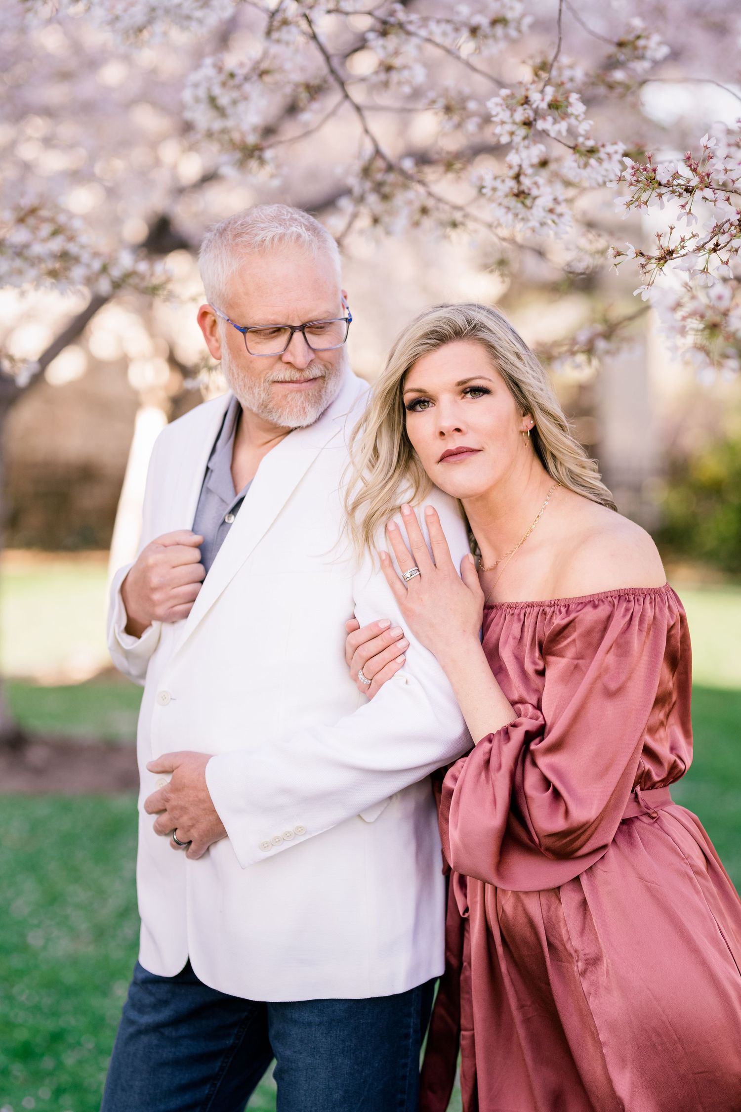 A couple poses together under blooming spring cherry blossom trees.