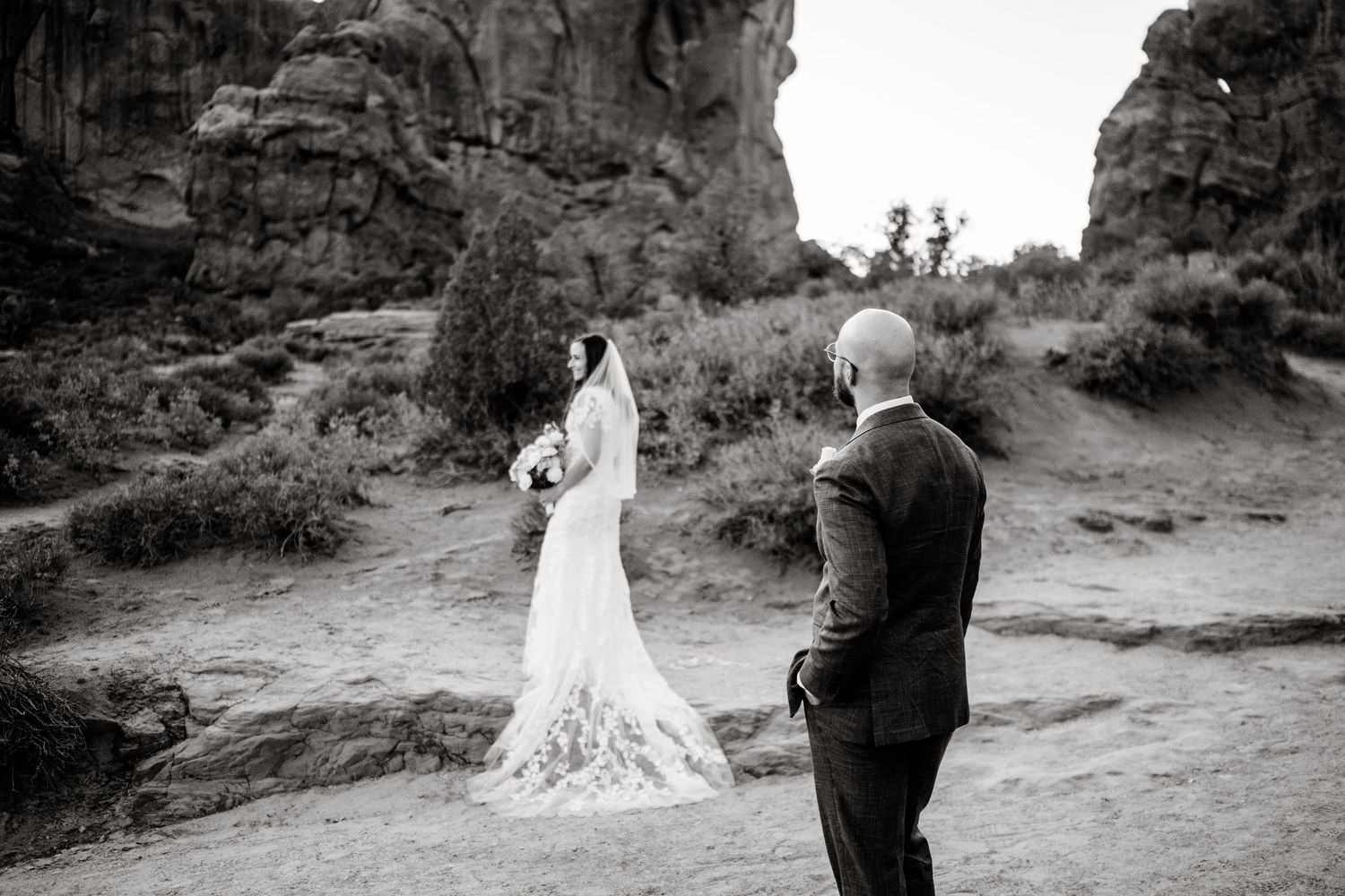 A black and white photo captures a wedding ceremony moment against towering desert cliffs.