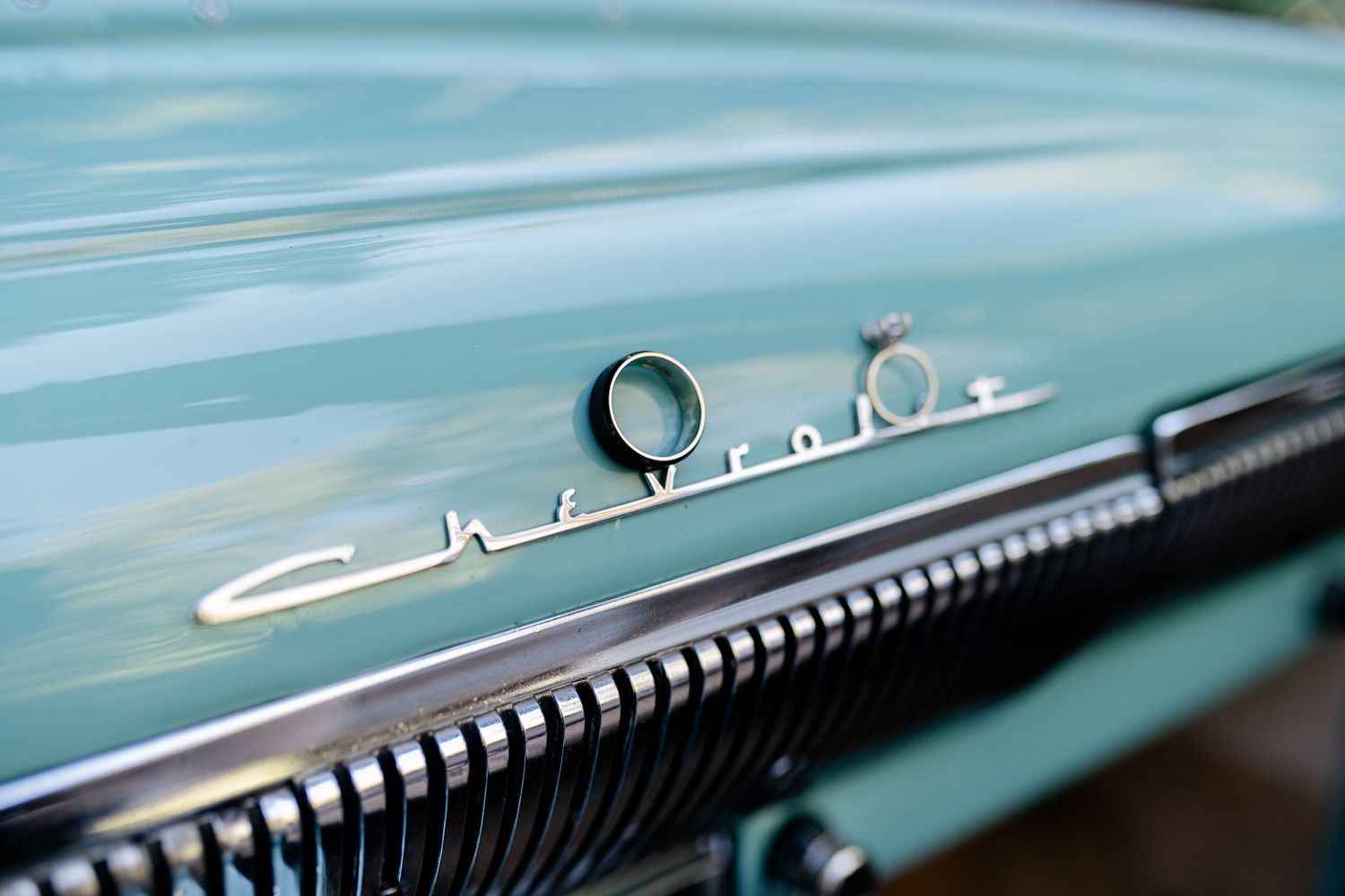 Close up detail of a vintage Chevrolet chrome emblem on a turquoise car hood.