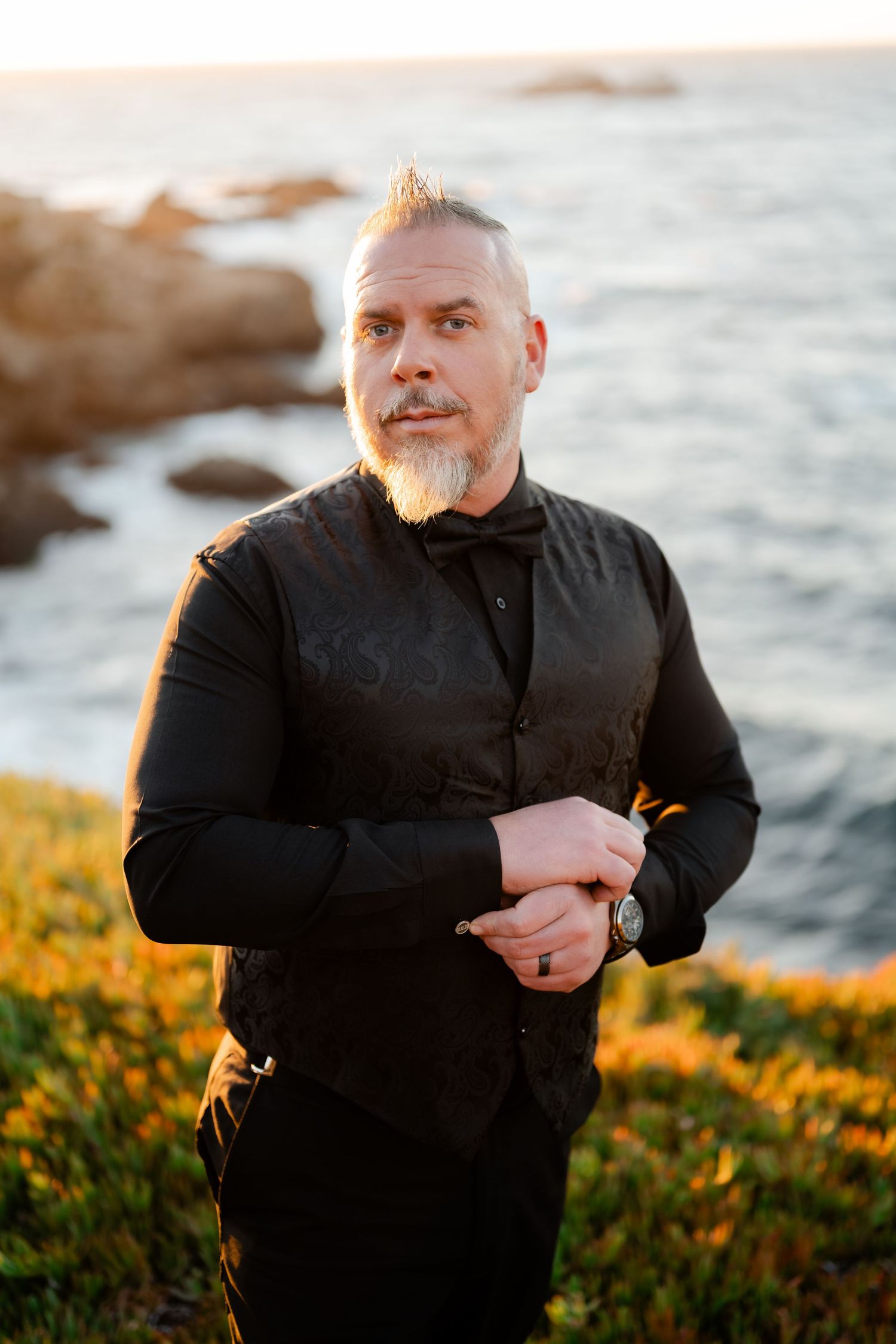 An elegant black formal outfit photographed against a golden sunset ocean landscape.