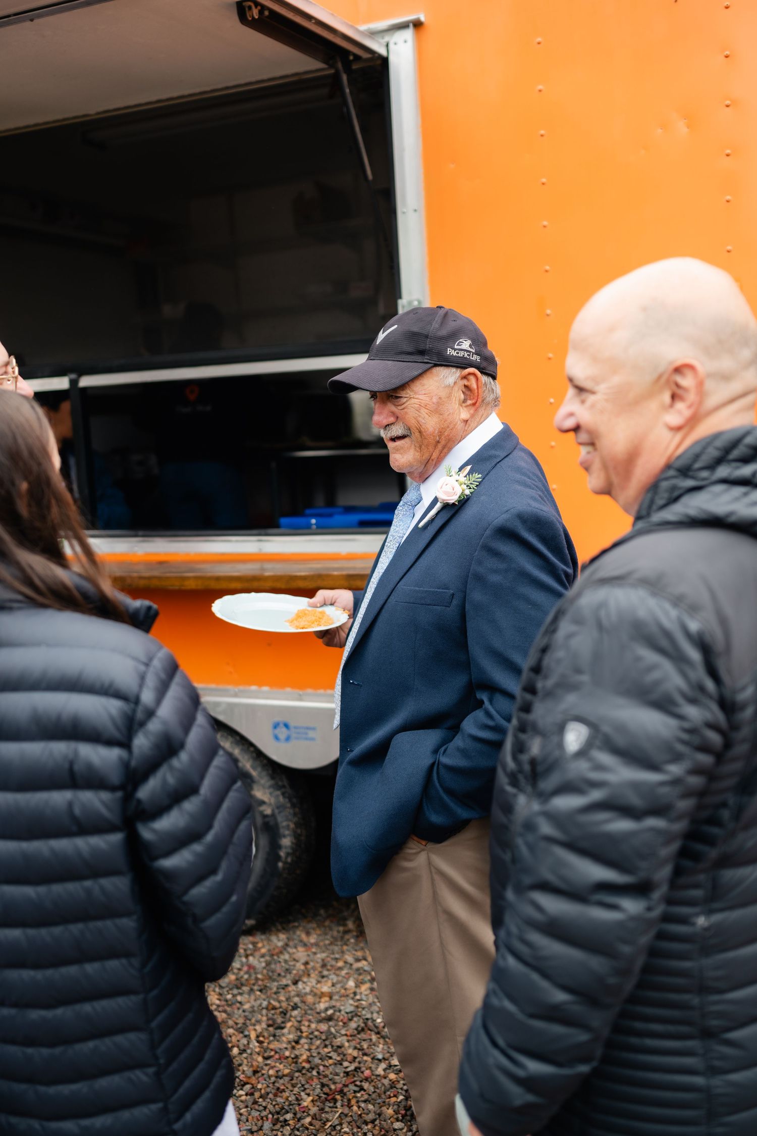 Line of guests getting food from an orange food truck at an outdoor event.
