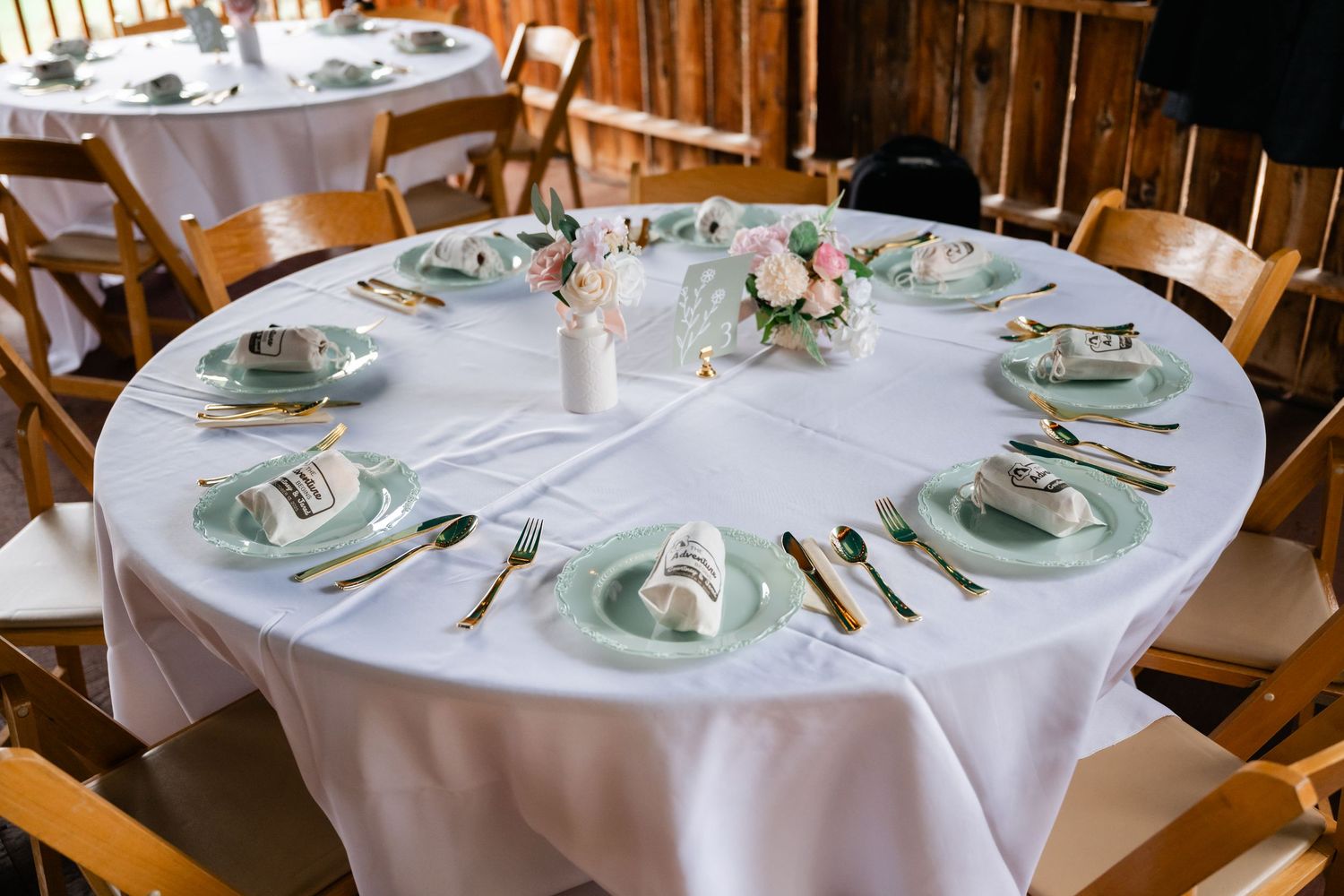 Elegant wedding reception tables set with white linens, place settings, and delicate green accents.