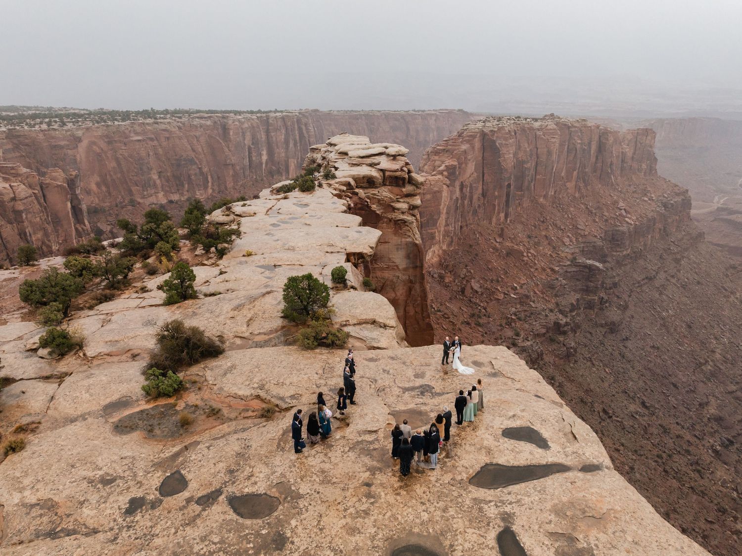 Wedding party standing at edge of majestic desert canyon during overcast day.