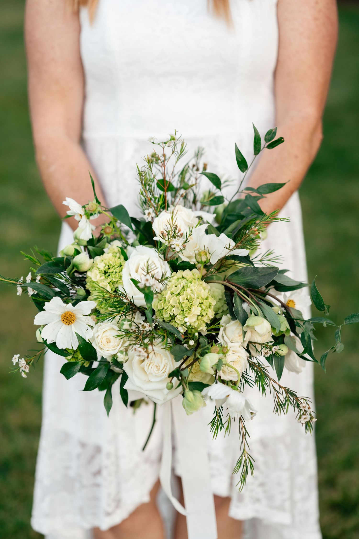 An elegant white and green wedding bouquet with daisies and mixed foliage.