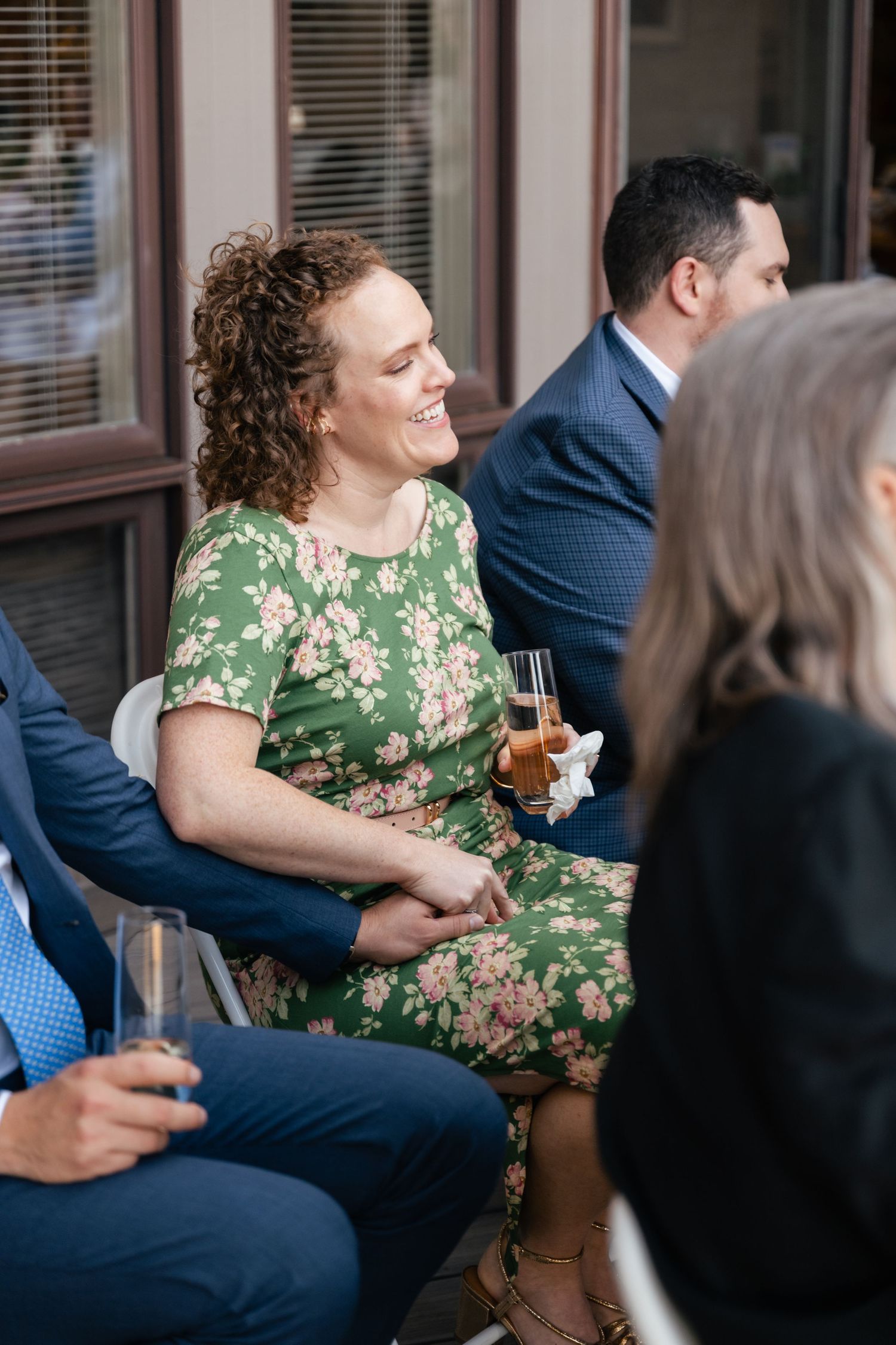 A guest in a floral dress enjoys refreshments during an outdoor wedding reception.
