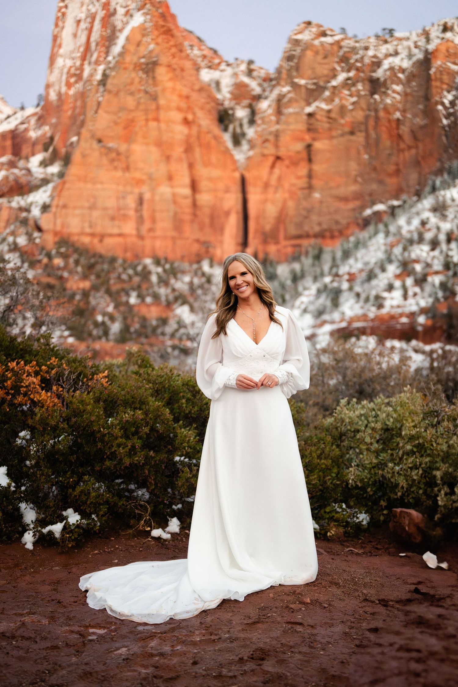 Bridal portraits with flowing white dress against red rock formations and snow.