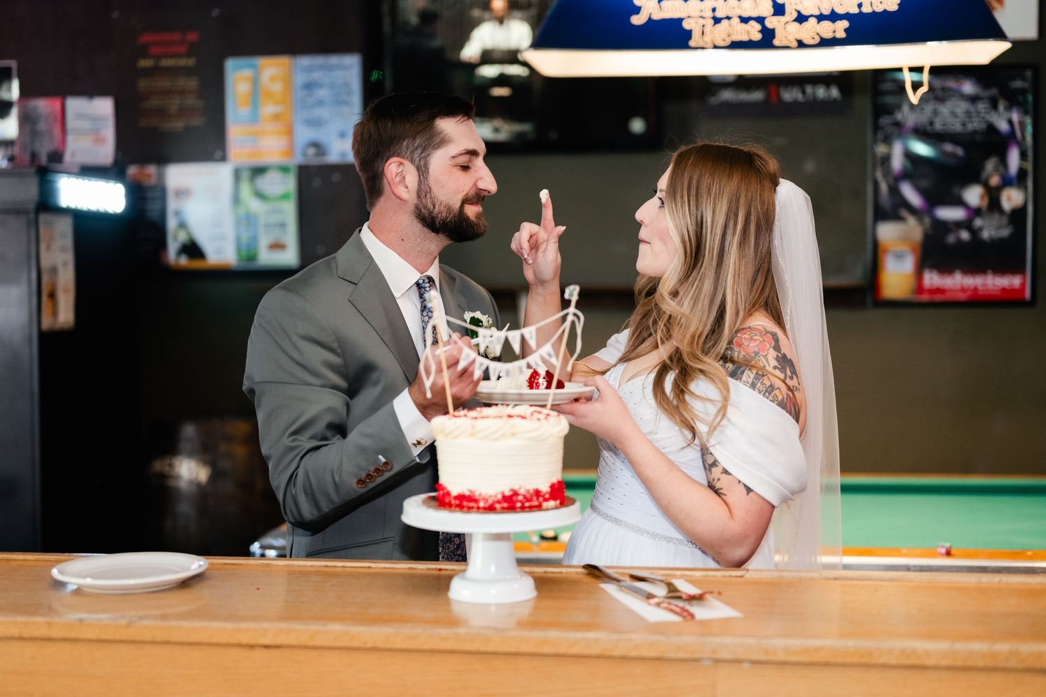 A couple enjoys their wedding cake together at a bar counter during their reception celebration.