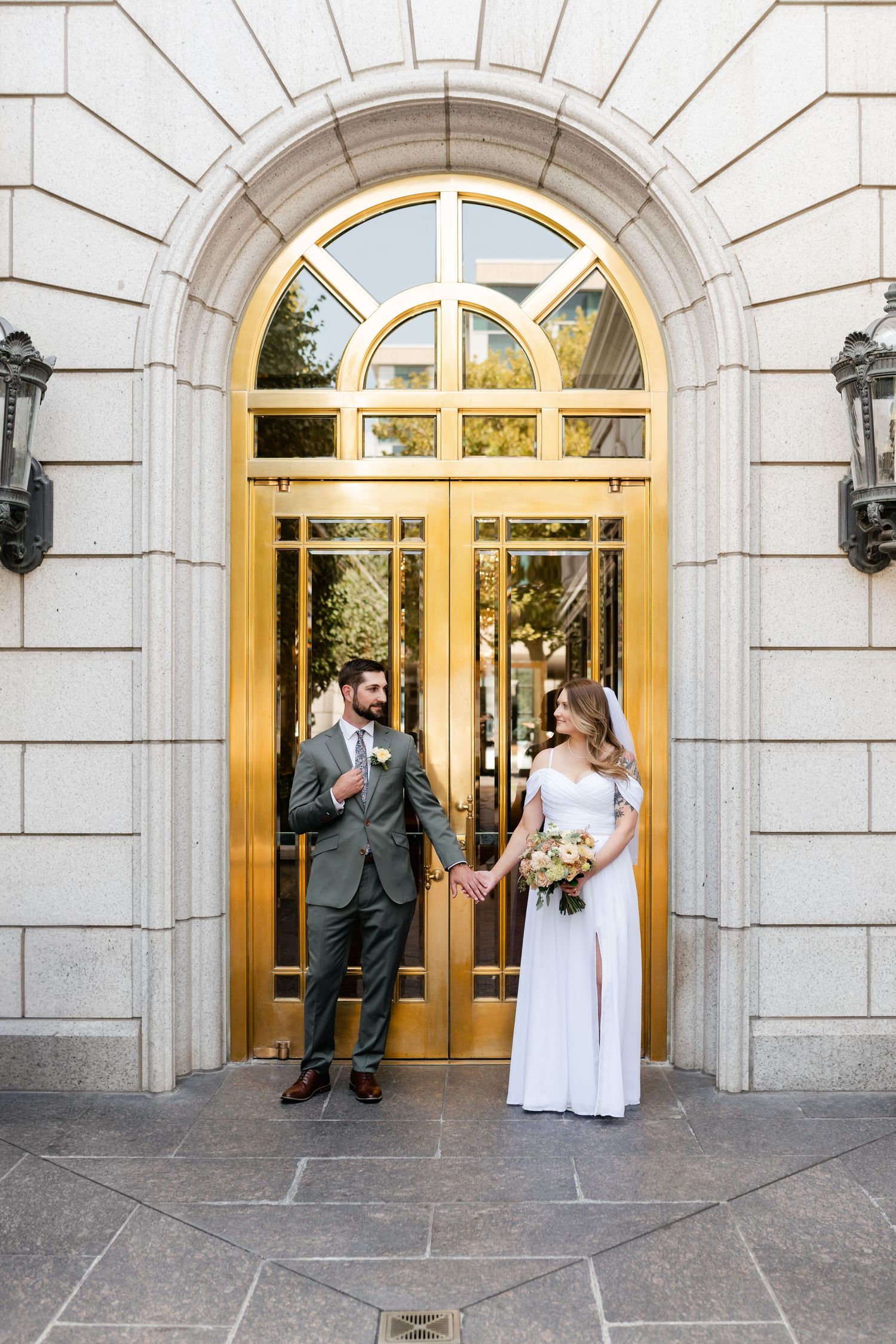 A couple stands in front of an elegant arched doorway with gold trim and lanterns during their wedding photoshoot.
