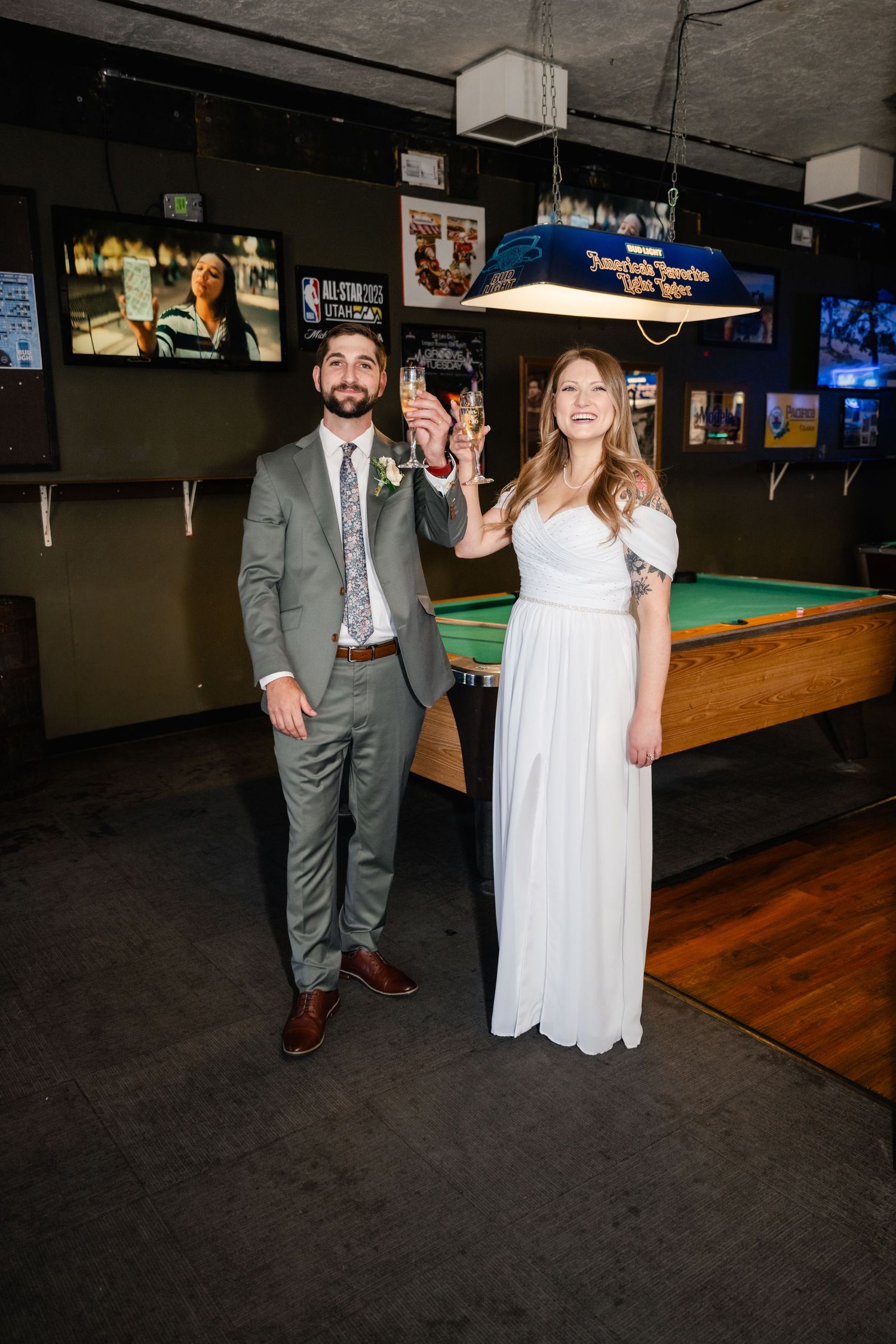 A newlywed couple poses playfully in front of pool tables at a bar venue.