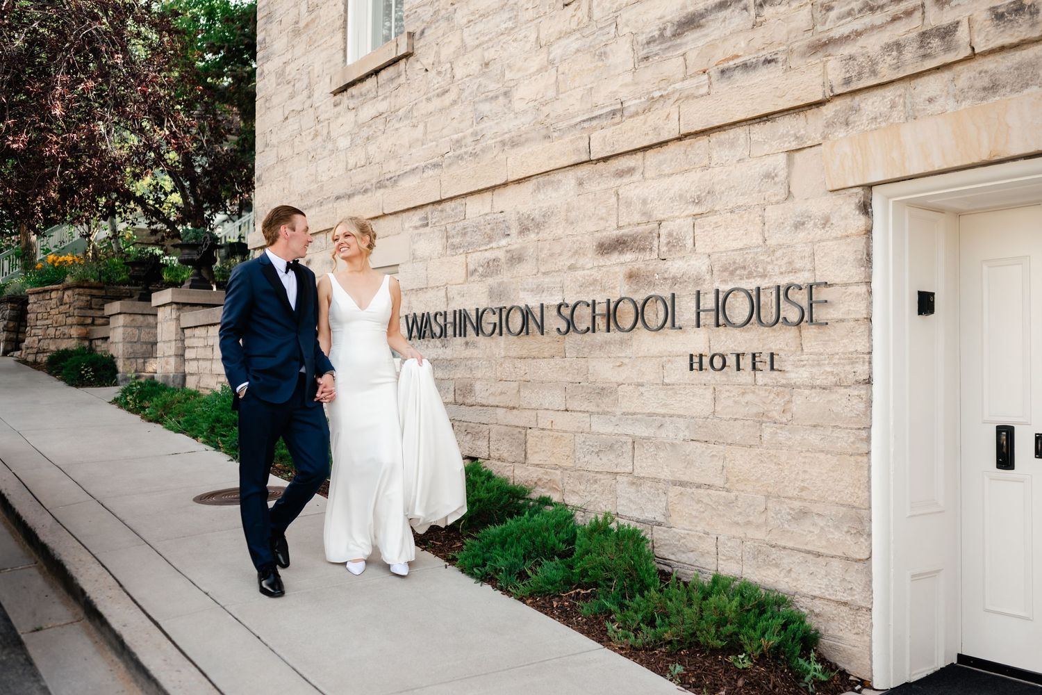Couple in wedding attire stands outside historic Wauwatosa School House Hotel.