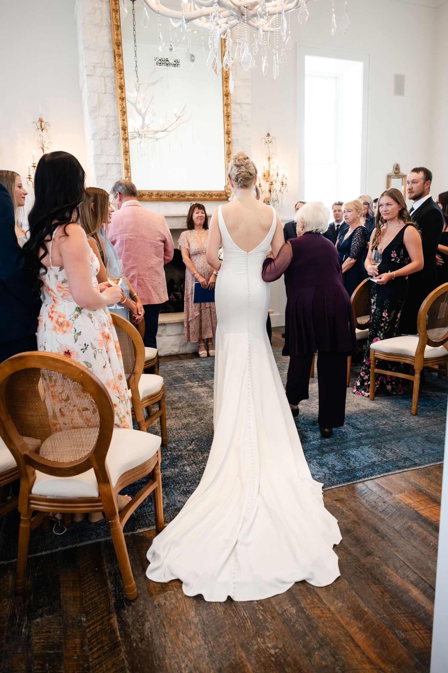 Wedding party gathering in an elegant room with chandeliers and vintage wooden floors.