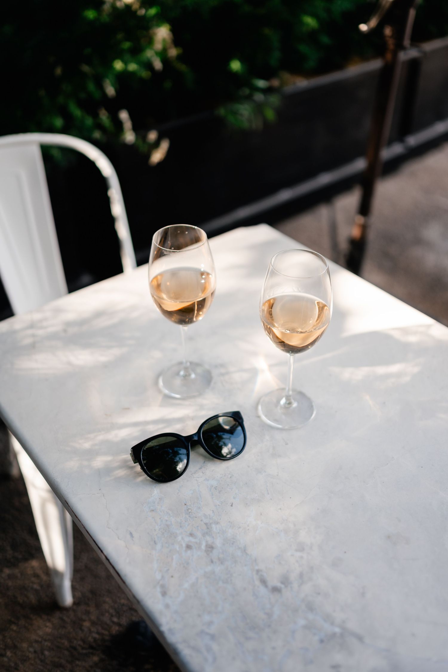 Two glasses of rosé wine and sunglasses on a white outdoor table in summer.