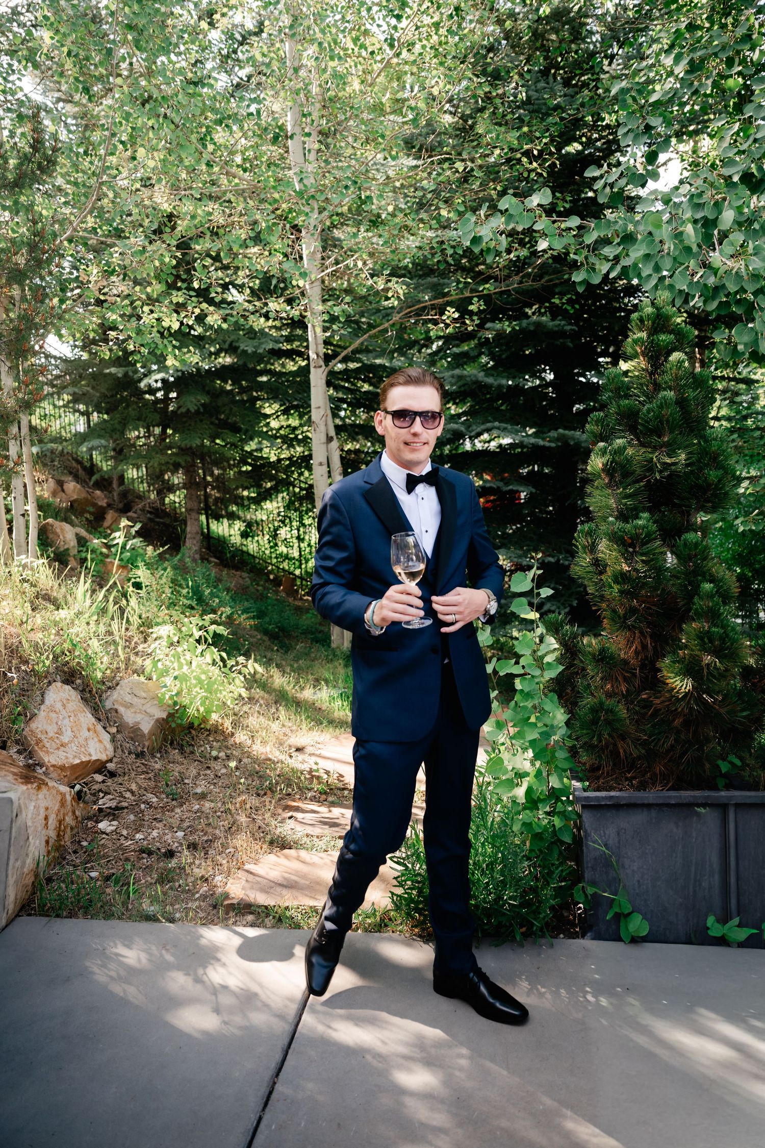 Person in a navy suit jumping playfully for photos on an outdoor patio.