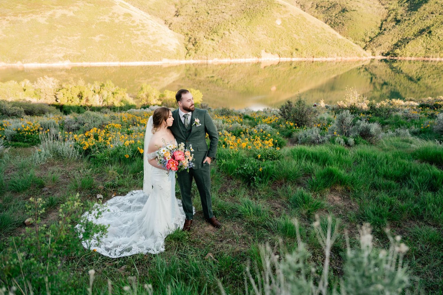 A couple stands together among wildflowers on a scenic hillside during golden hour.