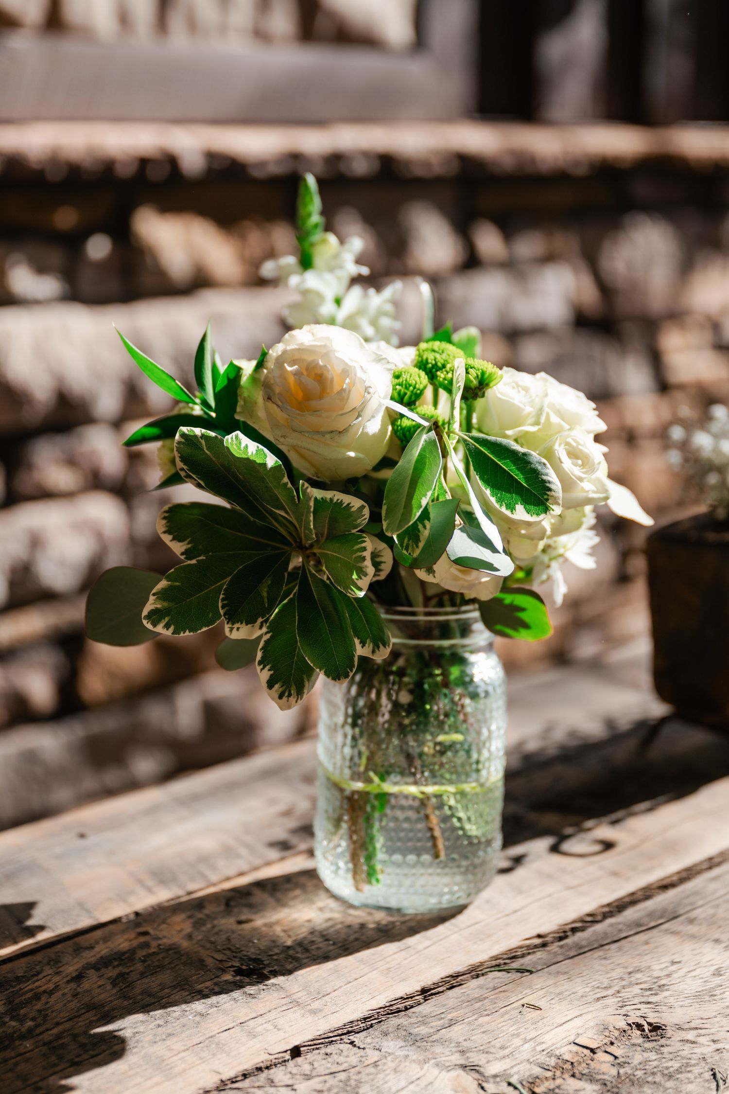 White flowers arranged in mason jars on a weathered wooden surface.