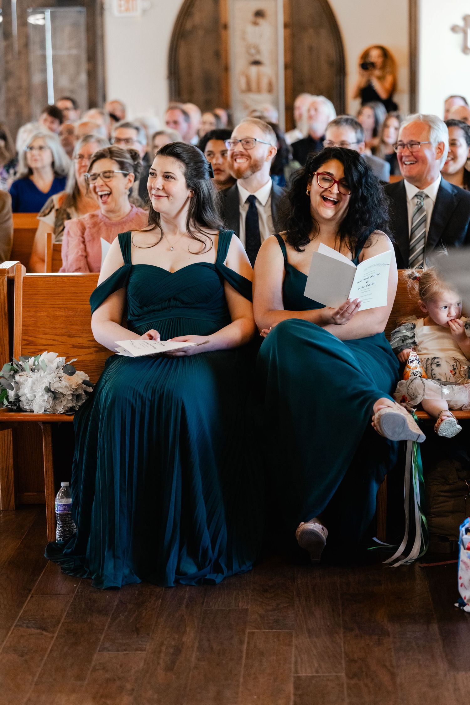 Wedding guests in navy blue dresses seated in church pews during ceremony.