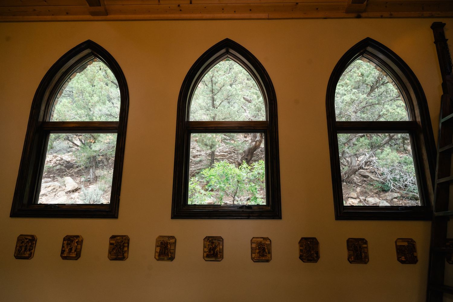 Arched windows line the top of a rustic wooden wall in a dimly lit room with natural light filtering through.