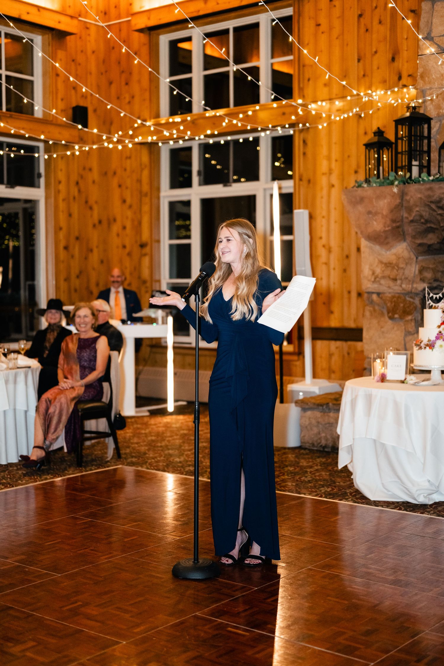 Couple shares a romantic dance on a polished wooden floor in a rustic barn venue decorated with twinkling lights.
