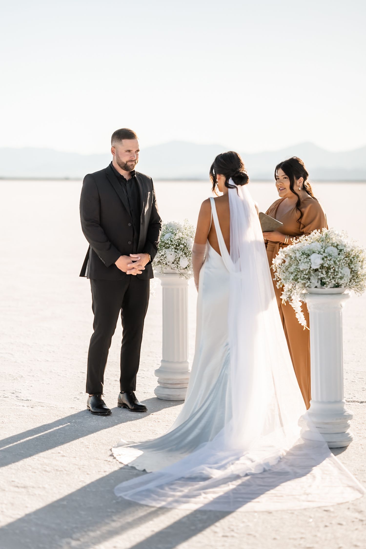 Wedding couple poses against white pillars on a bright salt flat landscape.