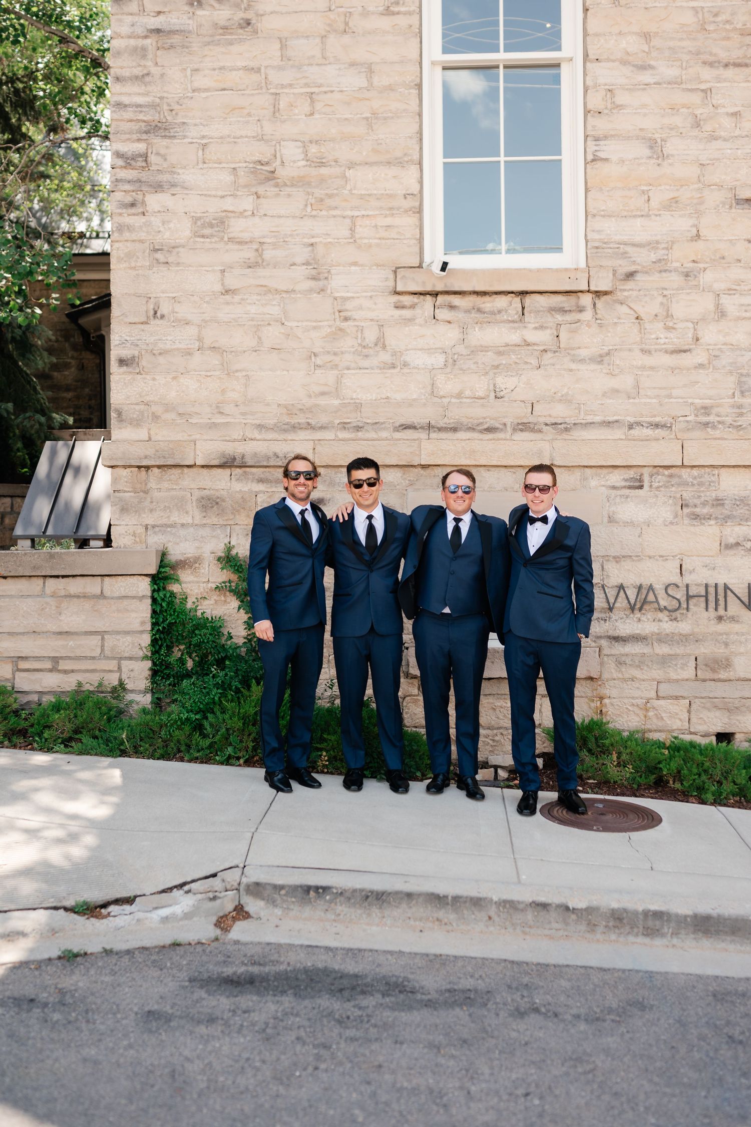 Four groomsmen in navy suits and sunglasses posing together outside the Washington School House Hotel on a wedding day in Park City.