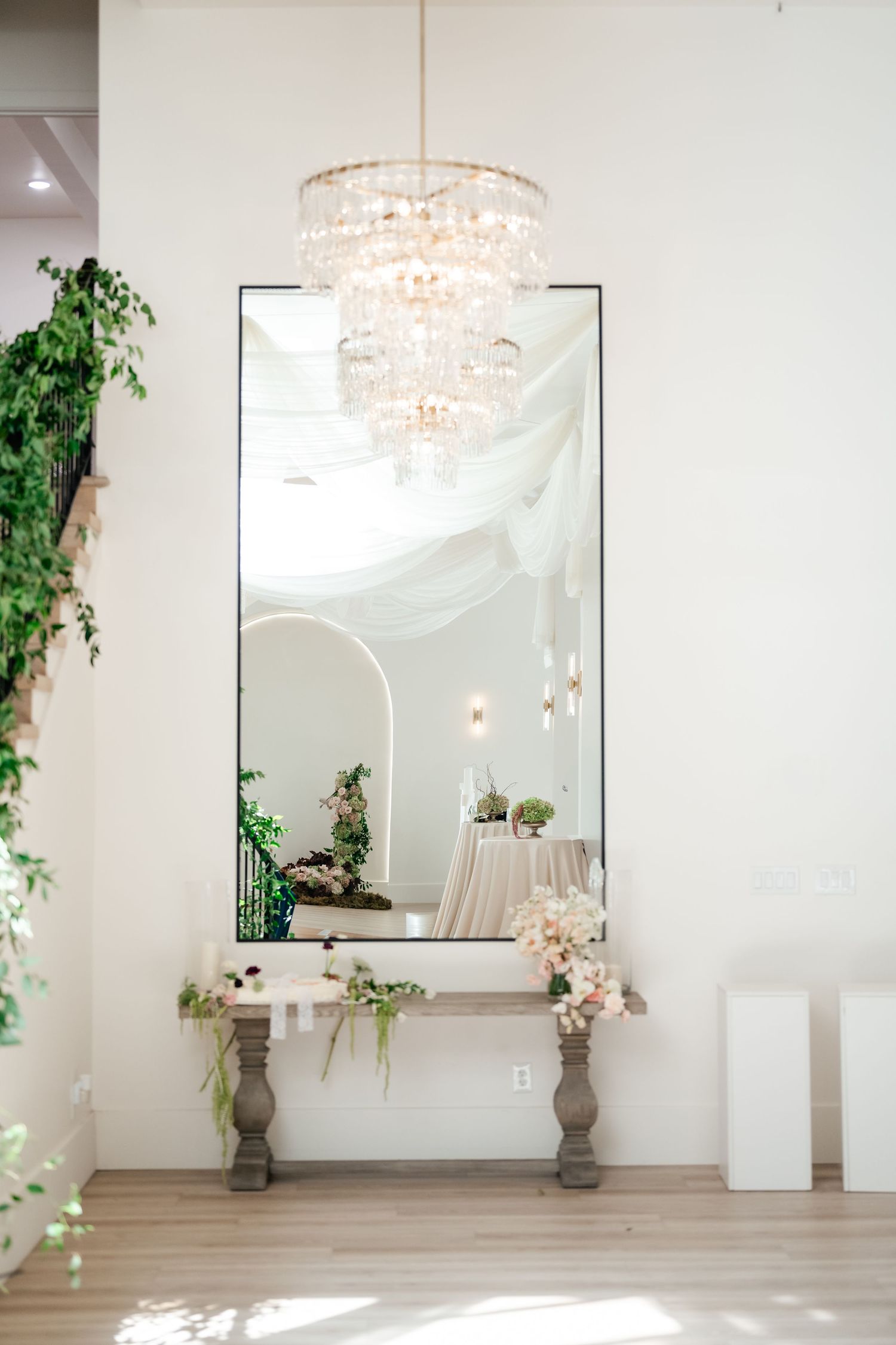Bright white wedding venue space with crystal chandeliers, mirrors, and trailing ivy decorations along the walls. Moments on Main in Payson